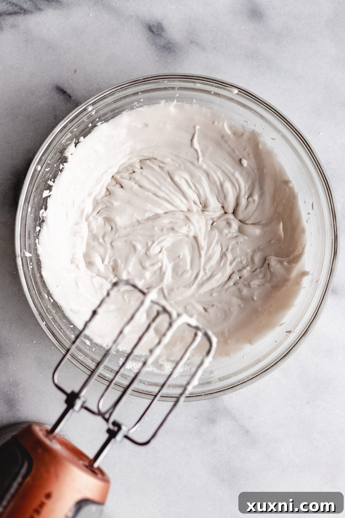 Thick, white vegan royal icing in a bowl, ready for piping onto a gingerbread house