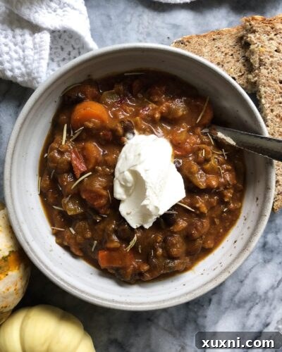 A close-up of a steaming bowl of pumpkin chili, showcasing its rich texture and vibrant colors.