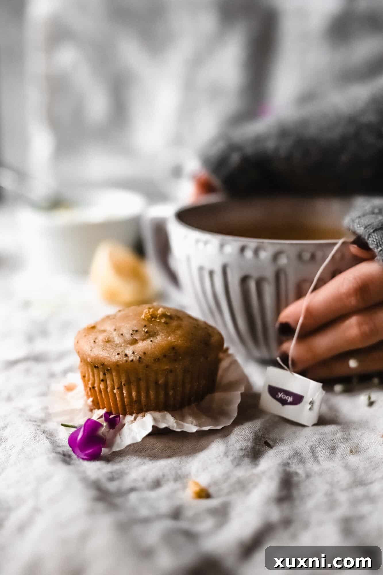 hand holding tea mug with lemon poppy seed muffin