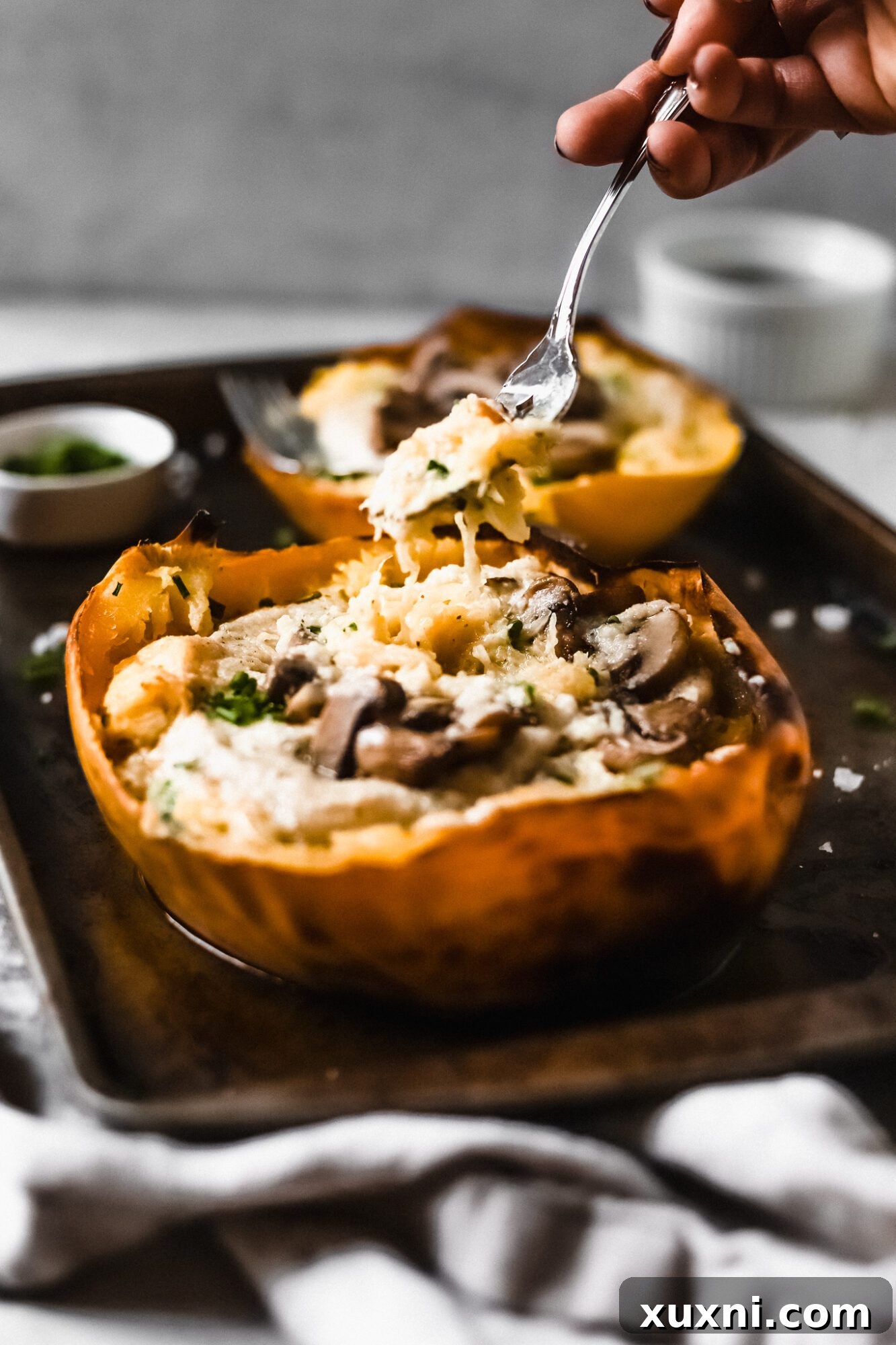 A fork lifting strands of spaghetti squash coated in luscious vegan Alfredo sauce, showcasing its creamy texture.