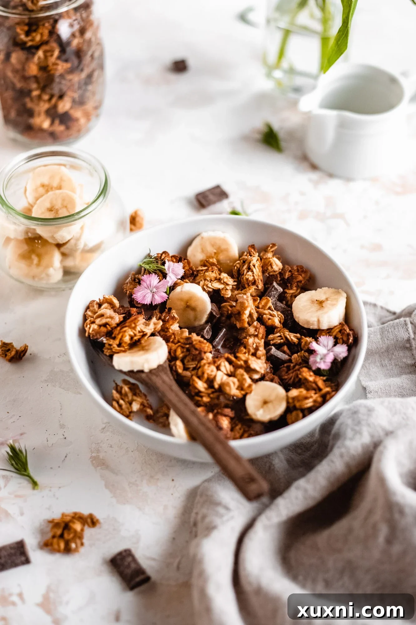 A beautifully styled scene featuring a bowl of banana bread oil-free granola, a patterned cloth, and a refreshing glass, ready for a cozy breakfast.
