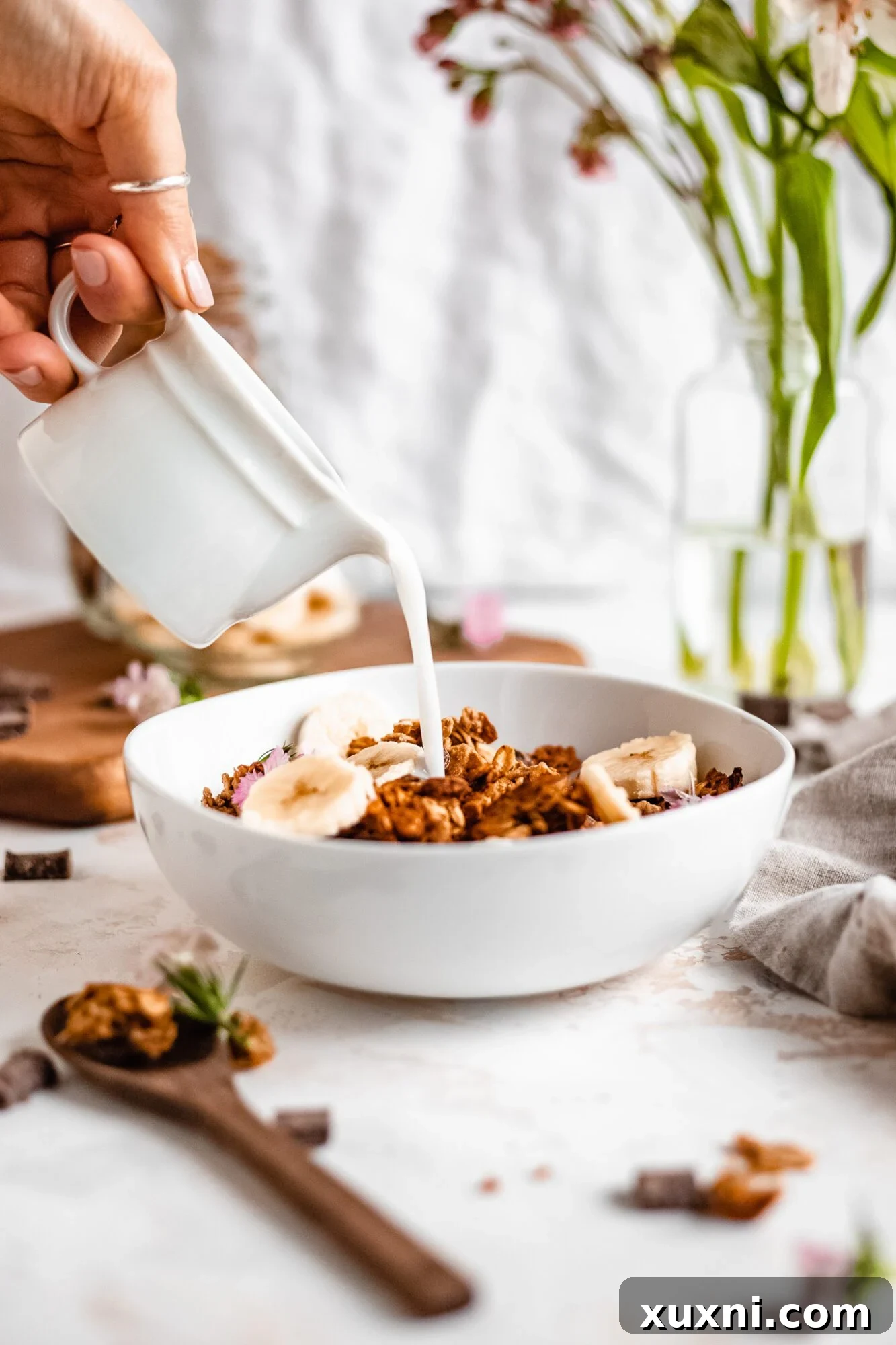 A hand gently pours creamy coconut milk into a bowl of crunchy granola, creating a perfect breakfast combination.