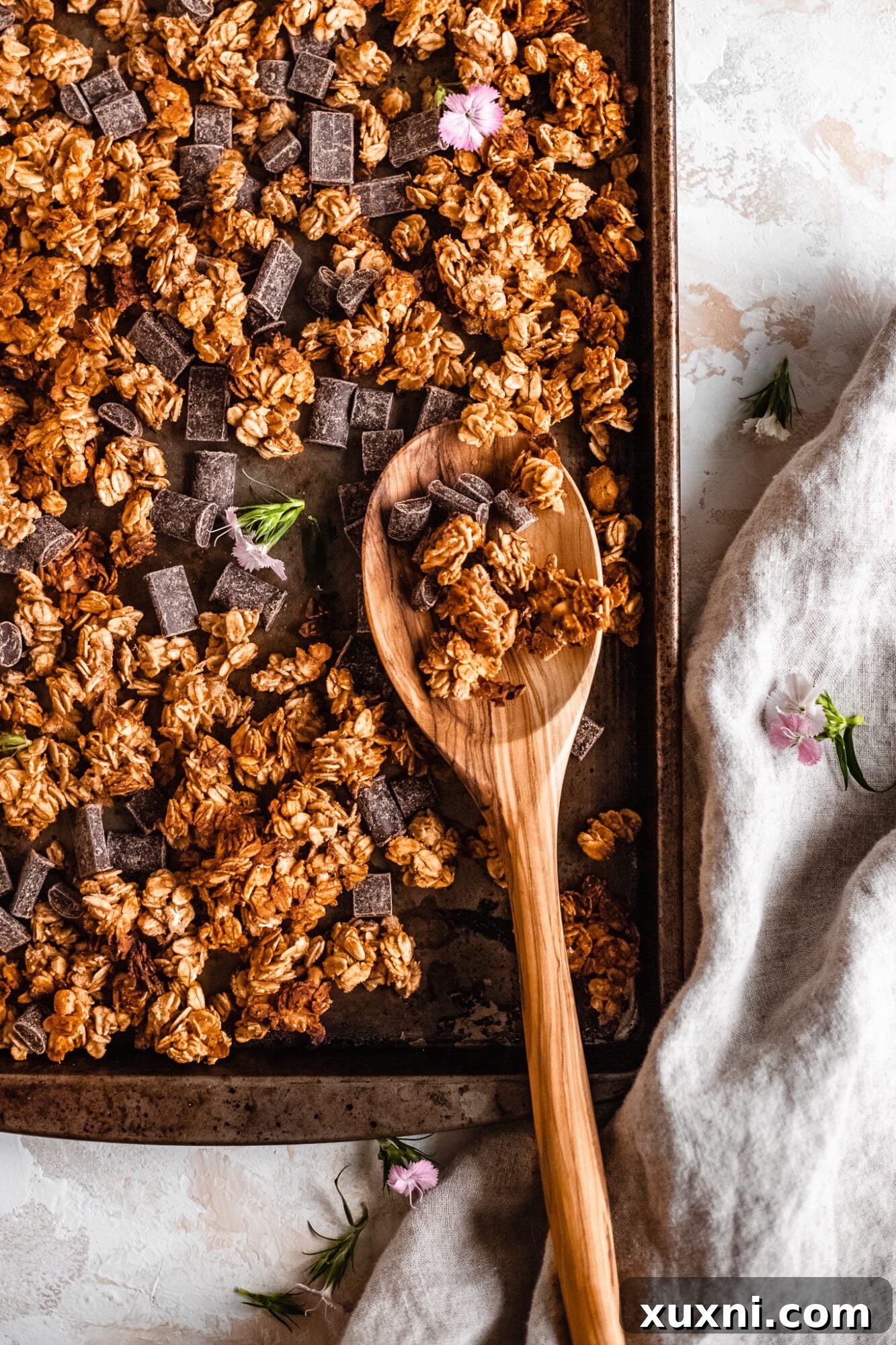 A wooden spoon scooping out perfectly clustered granola from a bowl, showcasing its crunchy texture.