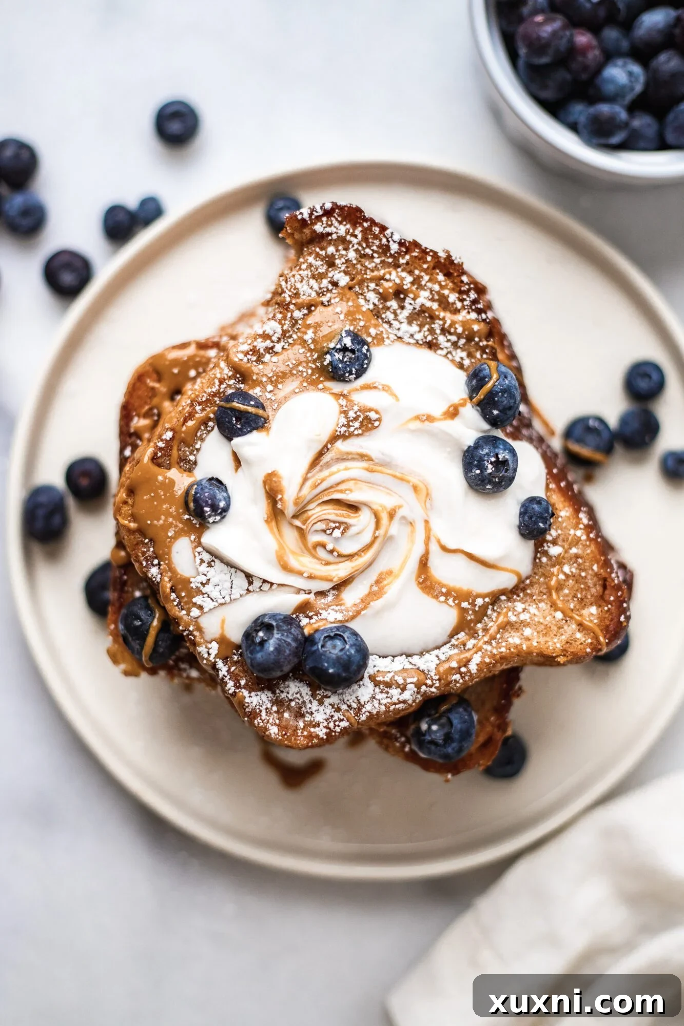 stack of vegan French toast with a swirl of coconut whipped cream and blueberries on top on a white plate.