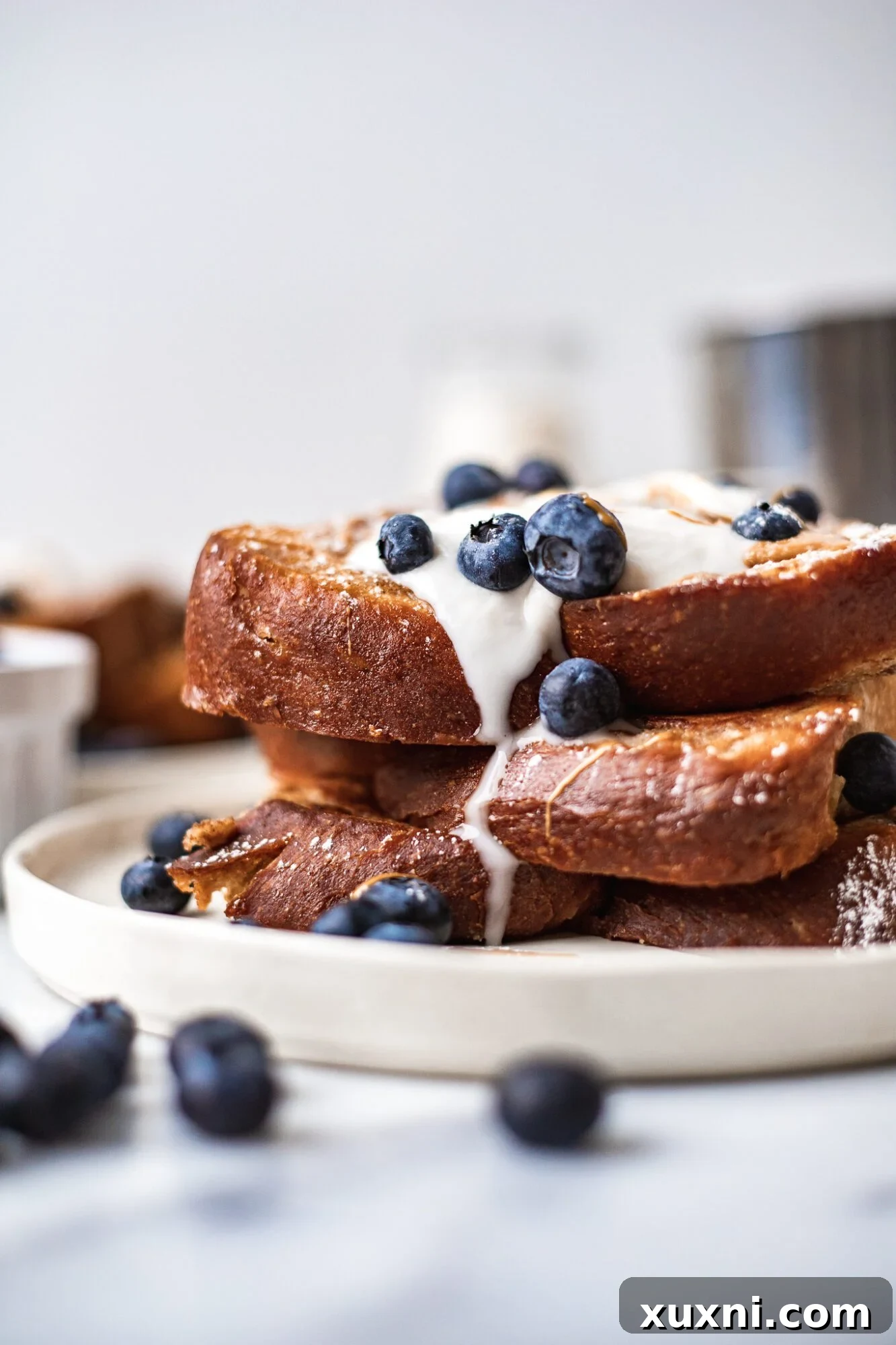 stack of vegan French toast close up with coconut whipped cream drizzling down it and blueberries. French toast is on a white plate.