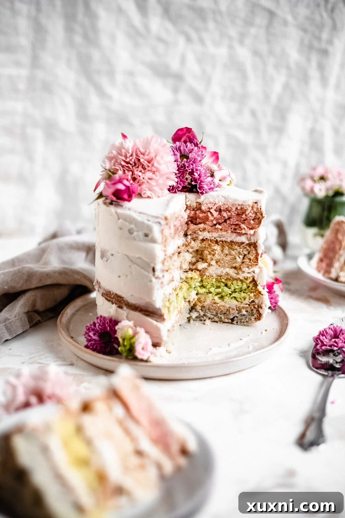 A vibrant vegan pastel layer cake on a plate, featuring a slice revealing colorful layers, adorned with delicate edible flowers.
