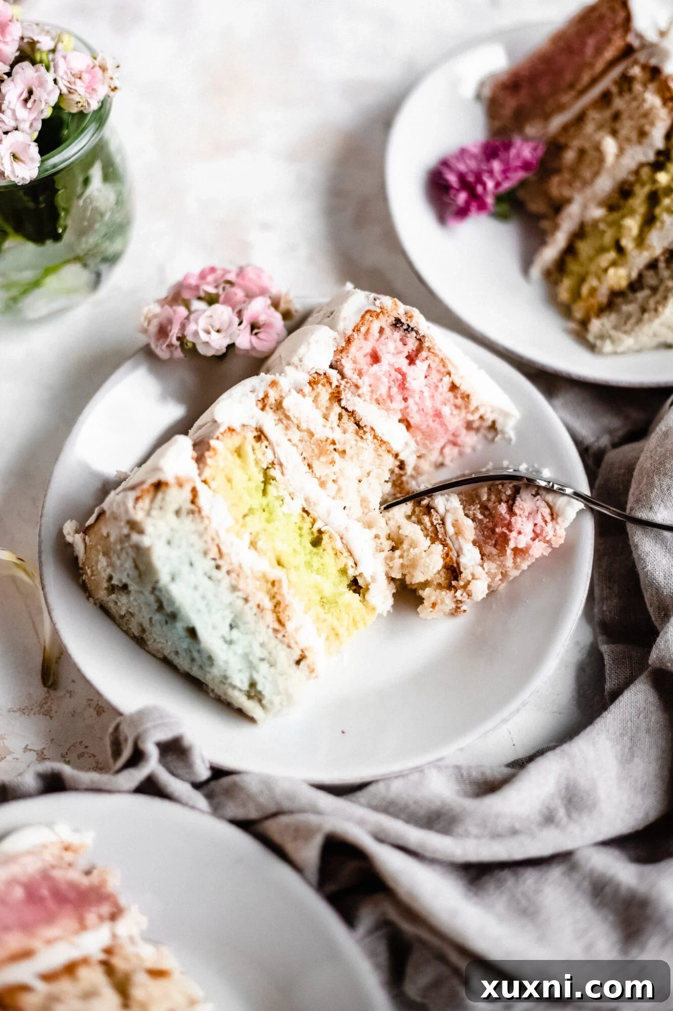 A fork taking a bite out of a slice of vegan pastel layer cake, emphasizing its tempting texture.
