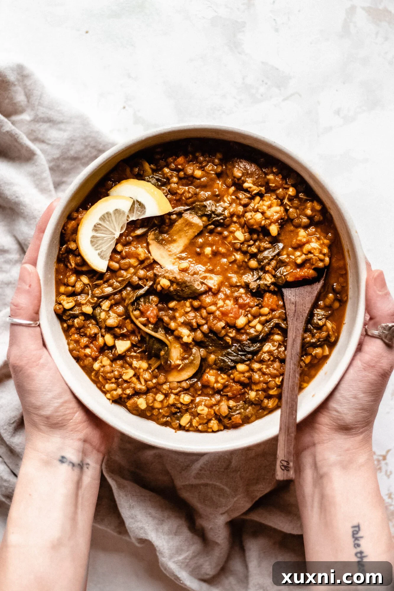 A hand holding a warm bowl of hearty vegan lentil soup, garnished with fresh herbs.