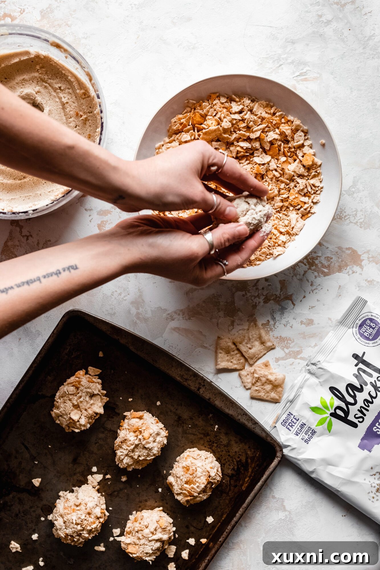 Hands dipping a soy-free vegan nugget into a bowl of bread crumbs, ensuring a complete and even coating.