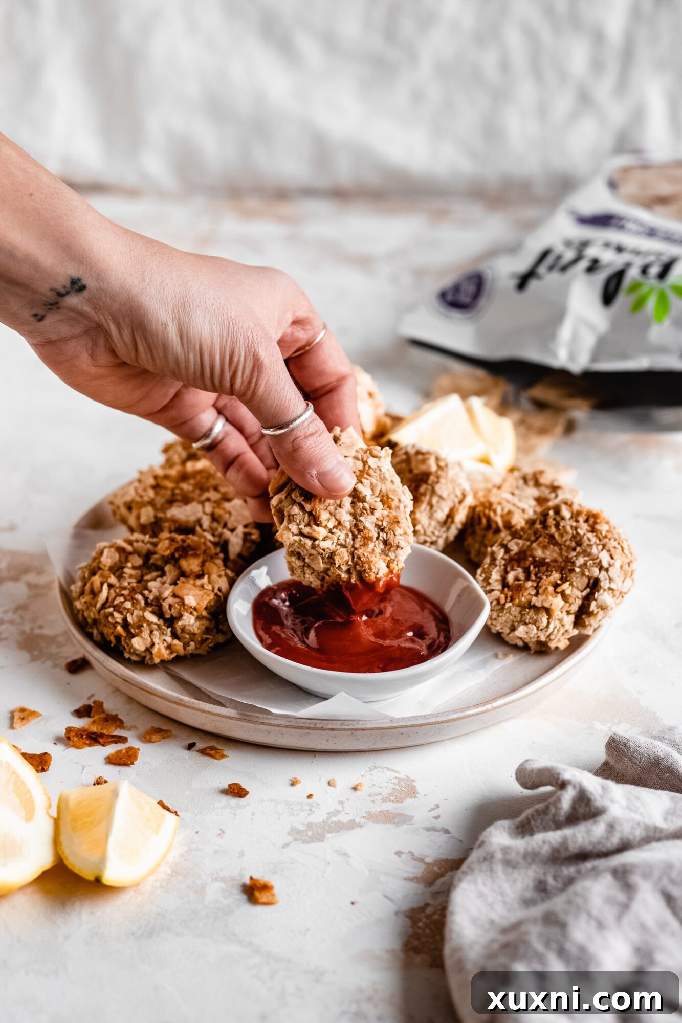 A hand dipping a crispy vegan cauliflower nugget into a bowl of vibrant red ketchup, inviting a delicious taste.