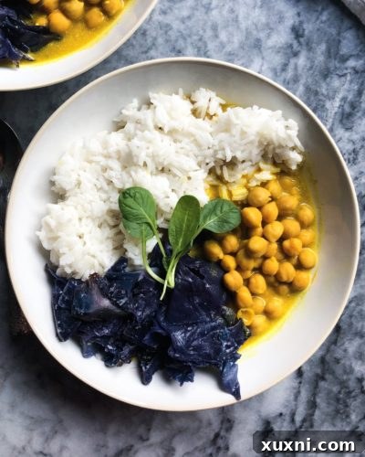 Creamy Vegan Coconut Chickpea Curry served with vibrant purple cabbage and jasmine rice on a wooden table.