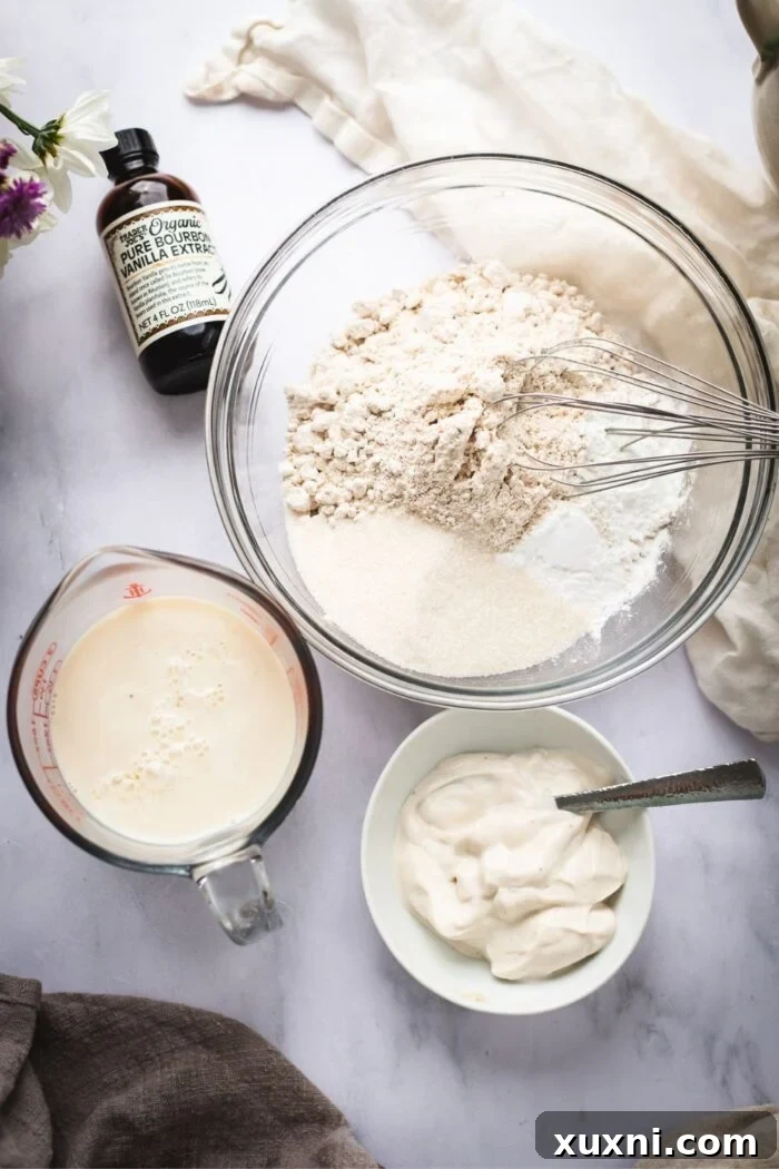 A collection of ingredients for vegan waffles including oat flour, applesauce, sugar, and non-dairy milk on a kitchen counter.