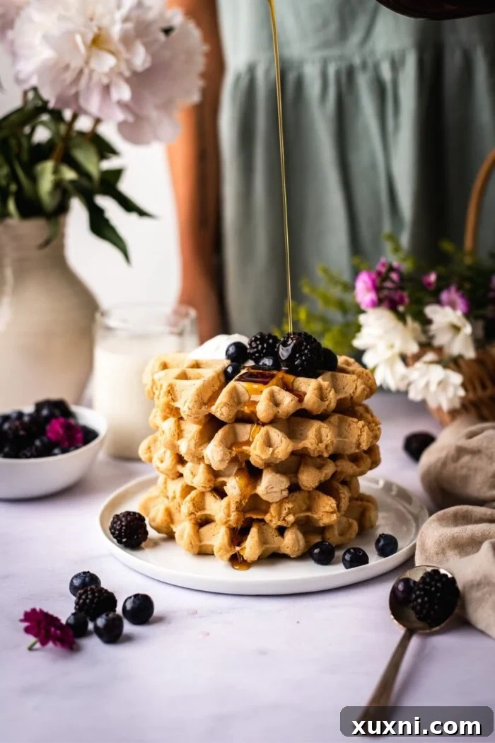 Close-up of fluffy vegan gluten-free waffles being drizzled with rich maple syrup, creating a mouth-watering cascade.