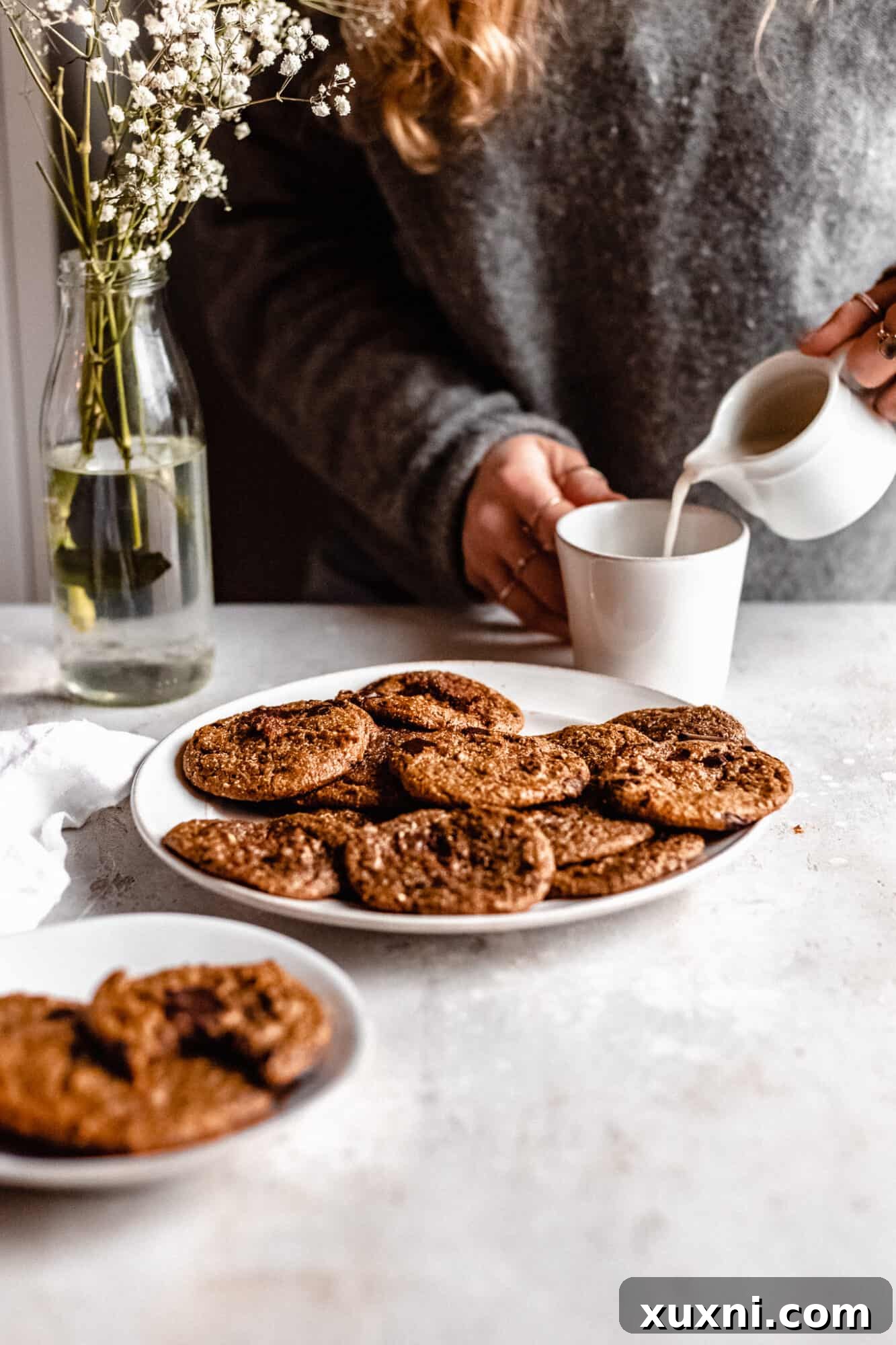 hand pouring cream into coffee cup with plate of cookies