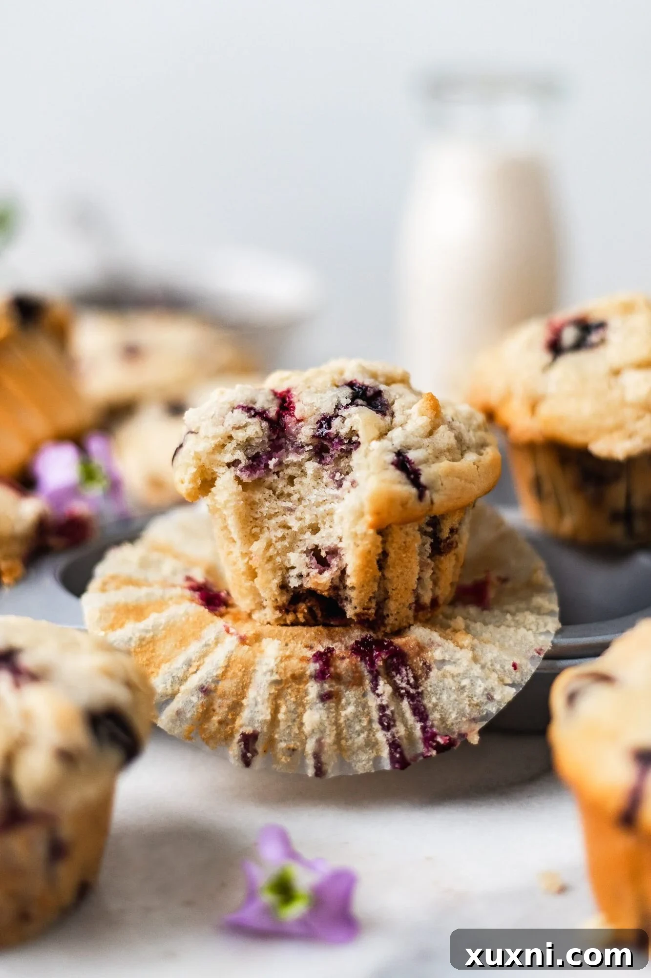 Tall, bakery-style vegan blueberry muffins with a golden crumble topping, showcasing their fluffy interior and juicy berries.