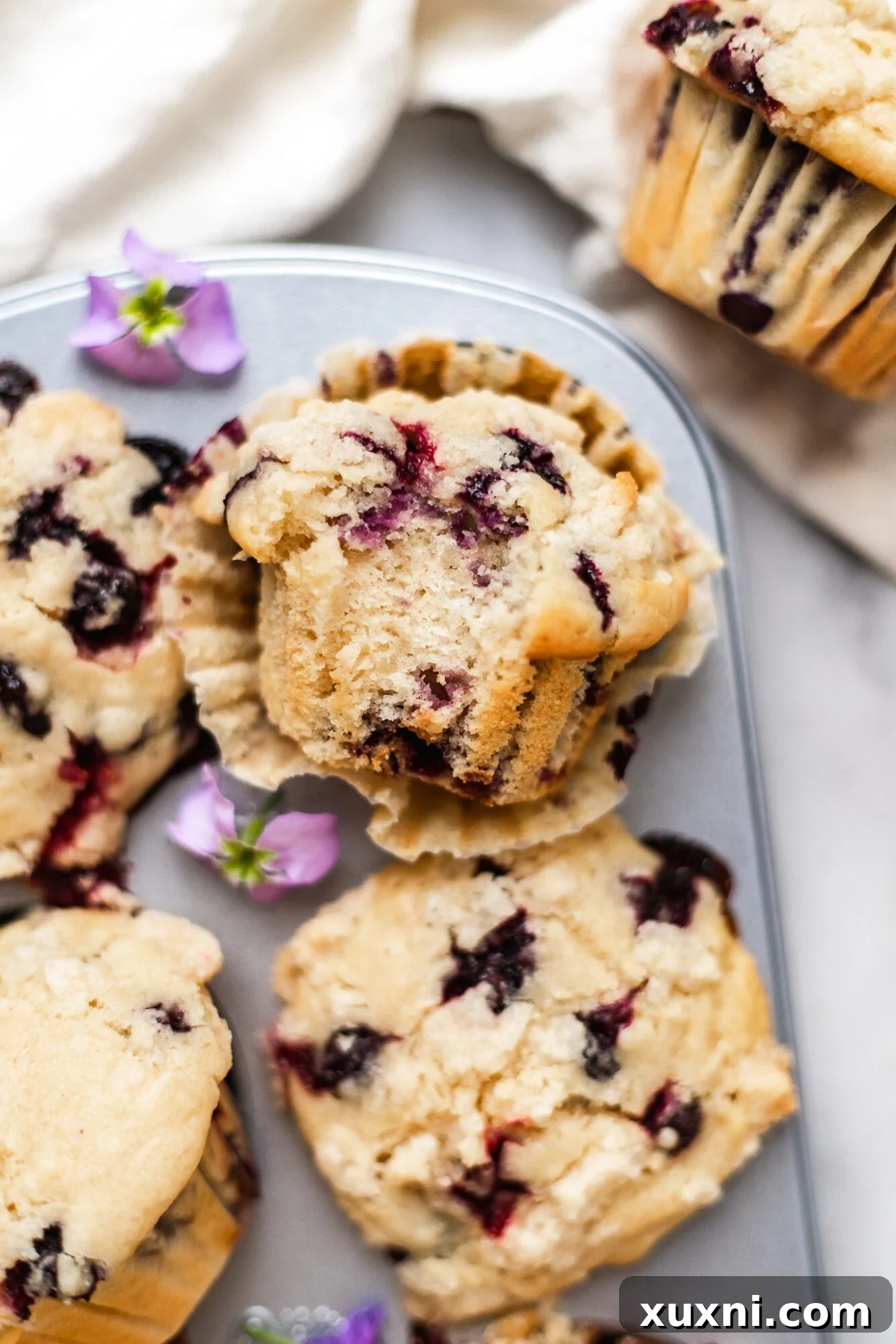A half-eaten vegan blueberry muffin in its liner, showing the moist crumb and juicy blueberries.