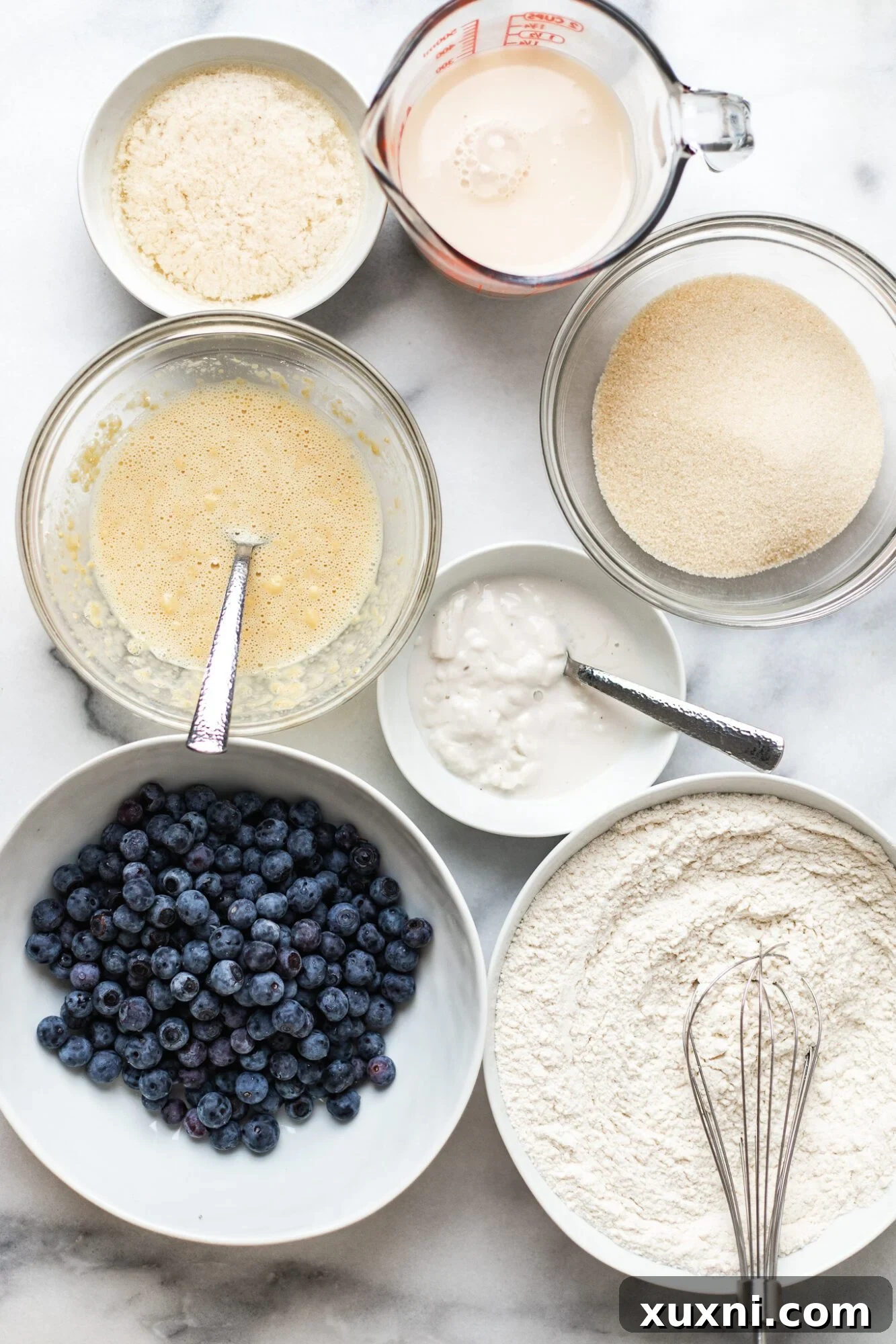A selection of vegan blueberry muffin ingredients laid out on a table, including flour, sugar, butter, and fresh blueberries.
