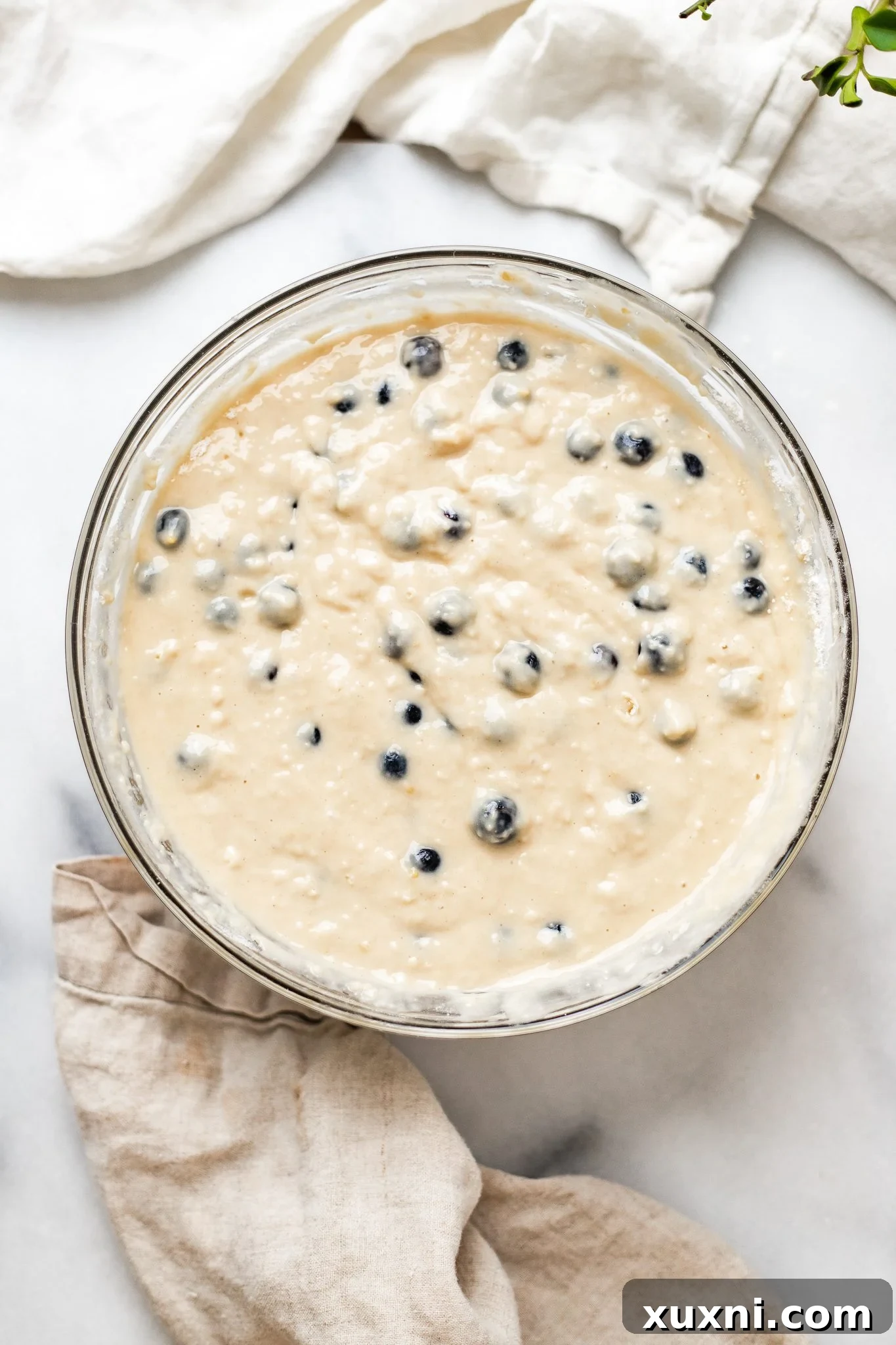Folding fresh blueberries into vegan muffin batter with a silicone spatula.