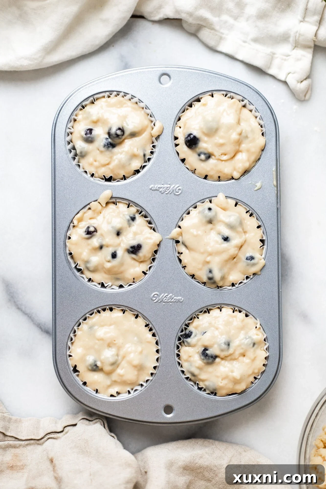 Vegan blueberry muffin batter being scooped into paper liners in a muffin tin.