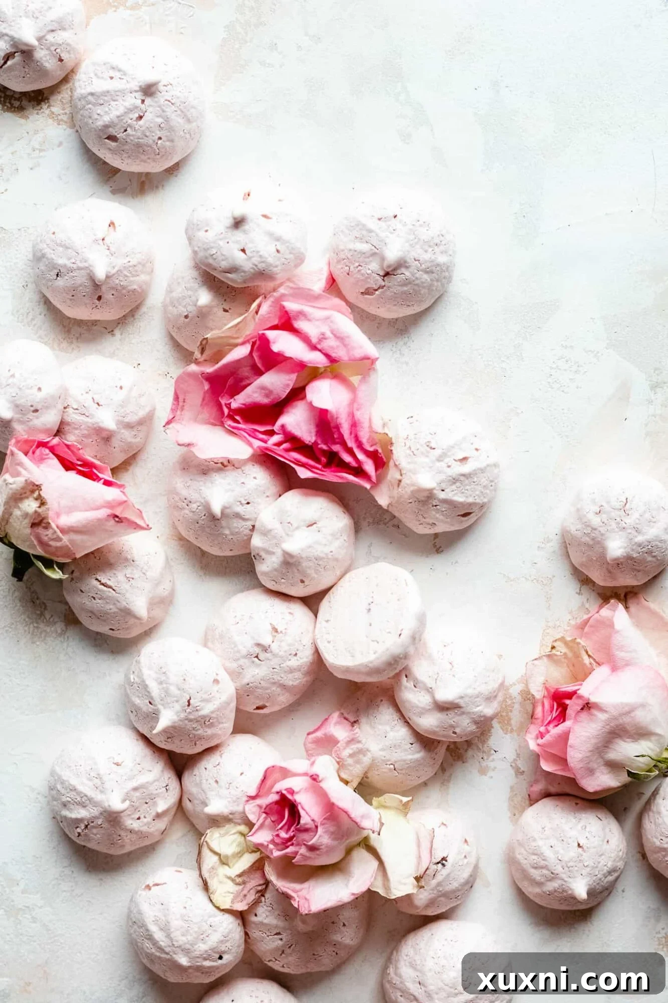 Delicate vegan meringue cookies adorned with edible rose petals, showcasing their airy texture and beautiful appearance.