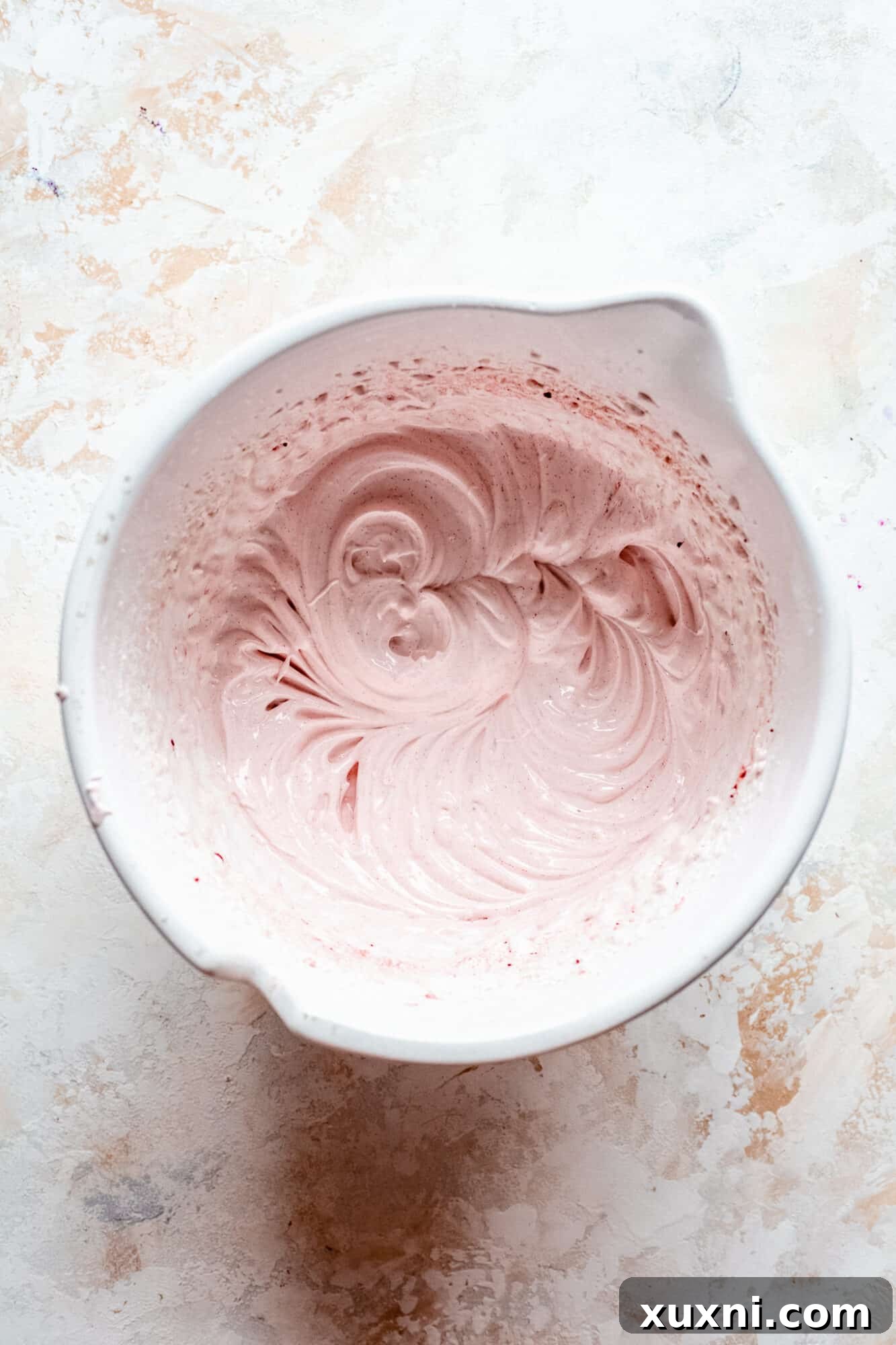 Fluffy vegan meringue, delicately tinted with food coloring, resting in a white mixing bowl.