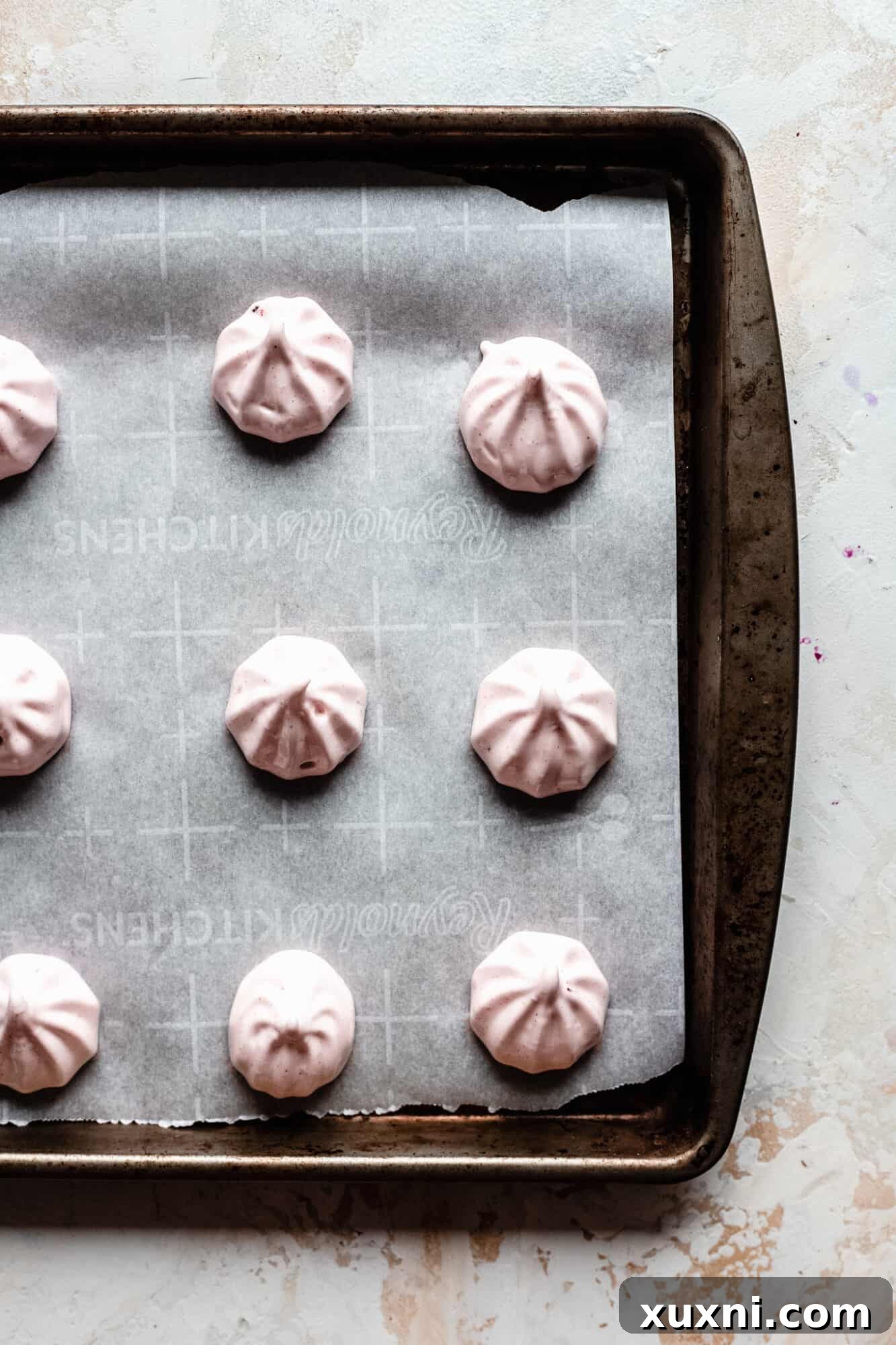 Neatly piped rows of vegan meringue cookies on a parchment-lined baking sheet, ready for the oven.