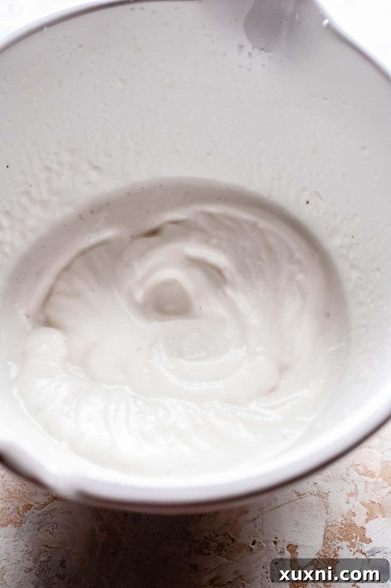 A generous scoop of fluffy vegan meringue in a pristine white bowl, showcasing its smooth texture.