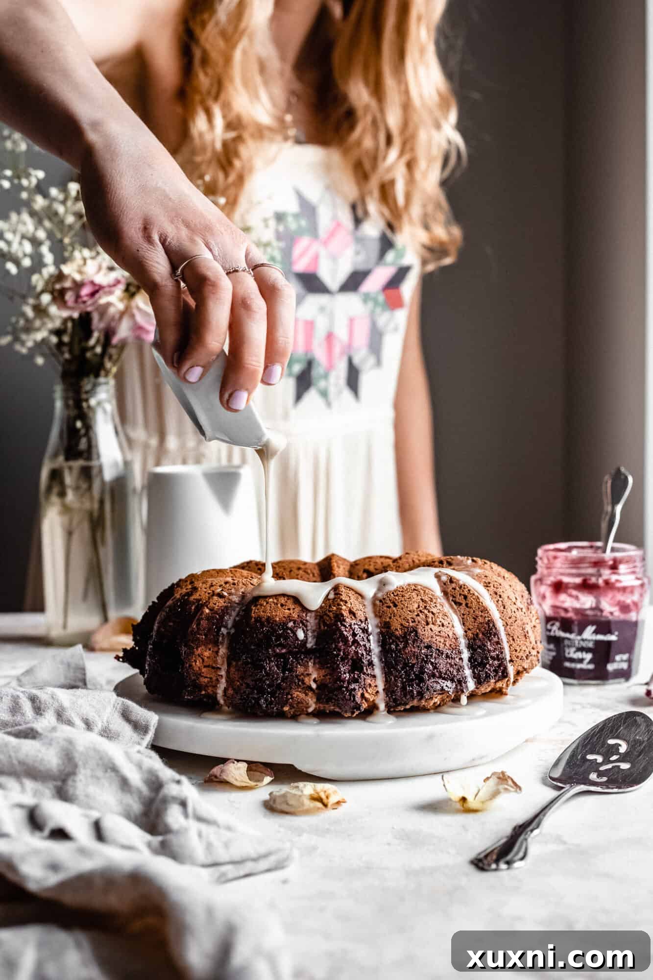 A hand drizzling a smooth glaze over the baked bundt cake.