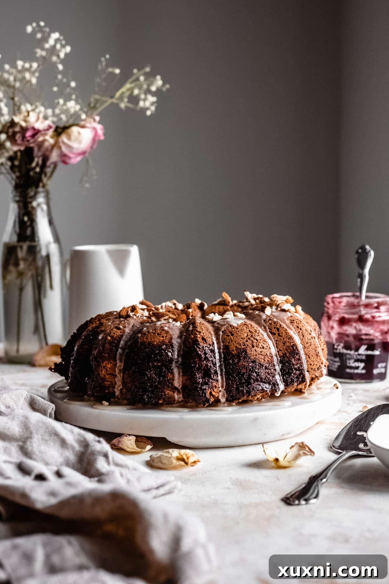 Vegan almond cherry bundt cake with a jar of Bonne Maman jam in the background.
