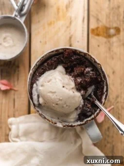 Vegan chocolate mug cake on a wooden table with a spoon eating it, topped with vegan ice cream.