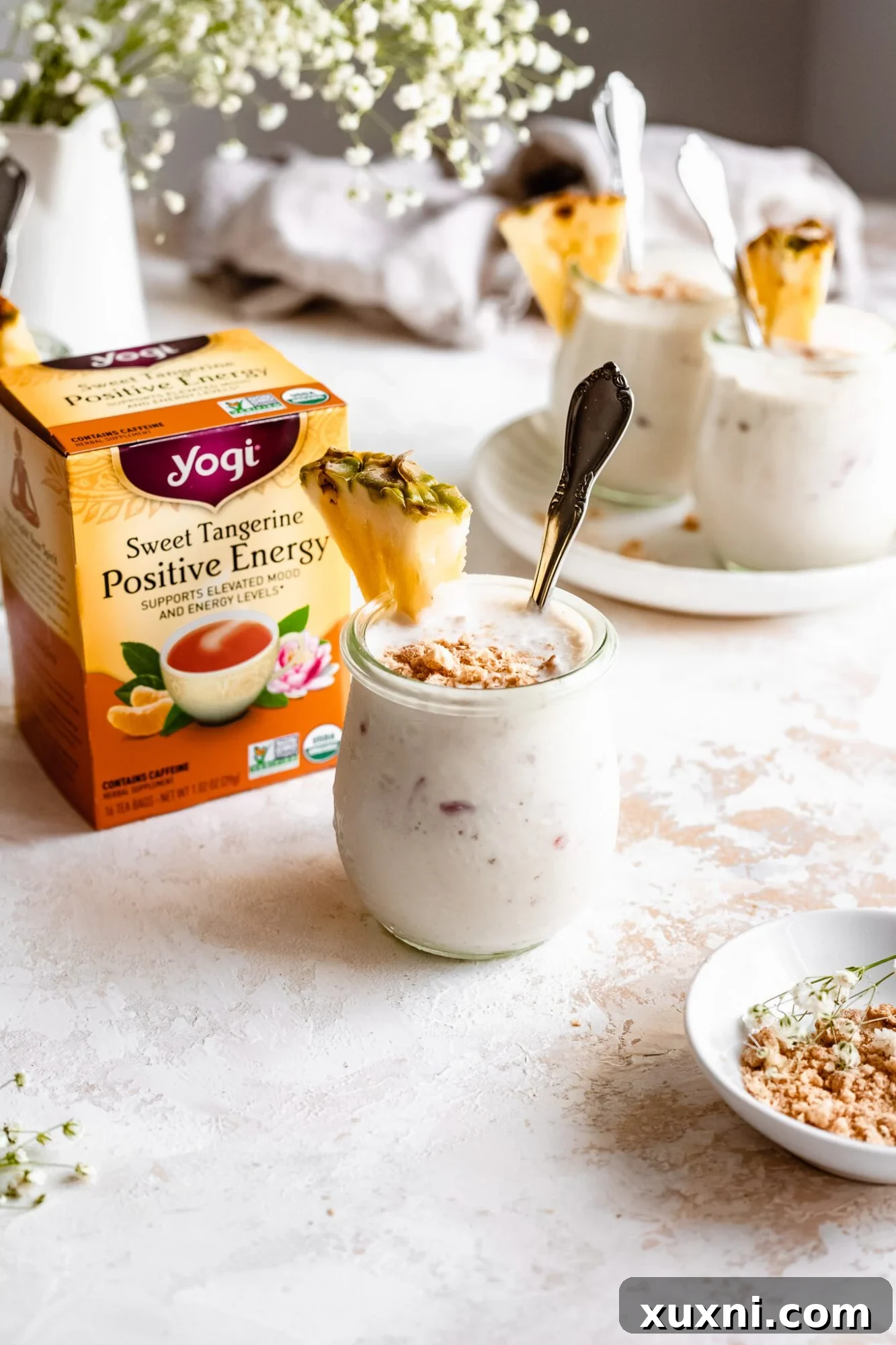 A jar of homemade vegan vanilla pudding stands beside a box of Yogi Sweet Tangerine Positive Energy tea, highlighting the key flavor infusion.