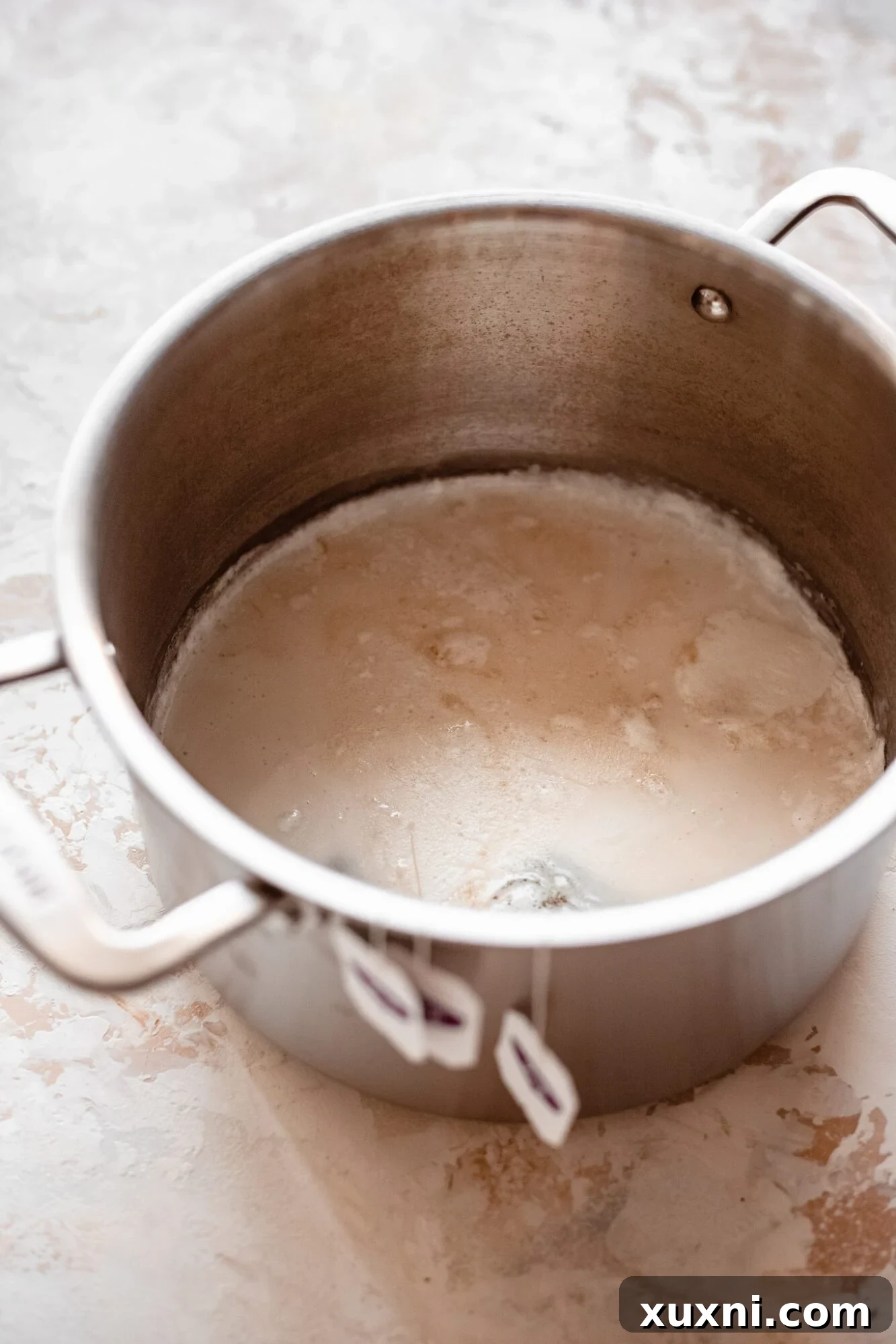 A large pot of rich coconut cream simmering on the stove, beginning the process of infusing flavors for the vegan vanilla pudding.