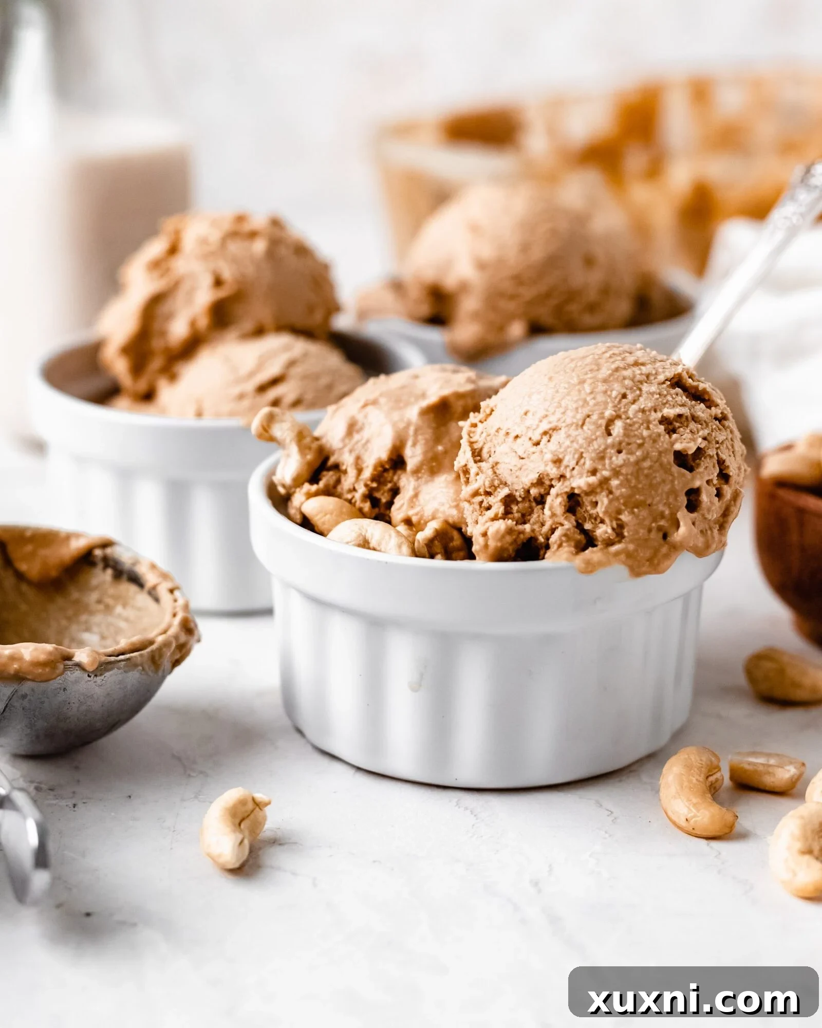 Multiple scoops of creamy vegan vanilla ice cream in a white bowl, with a spoon.