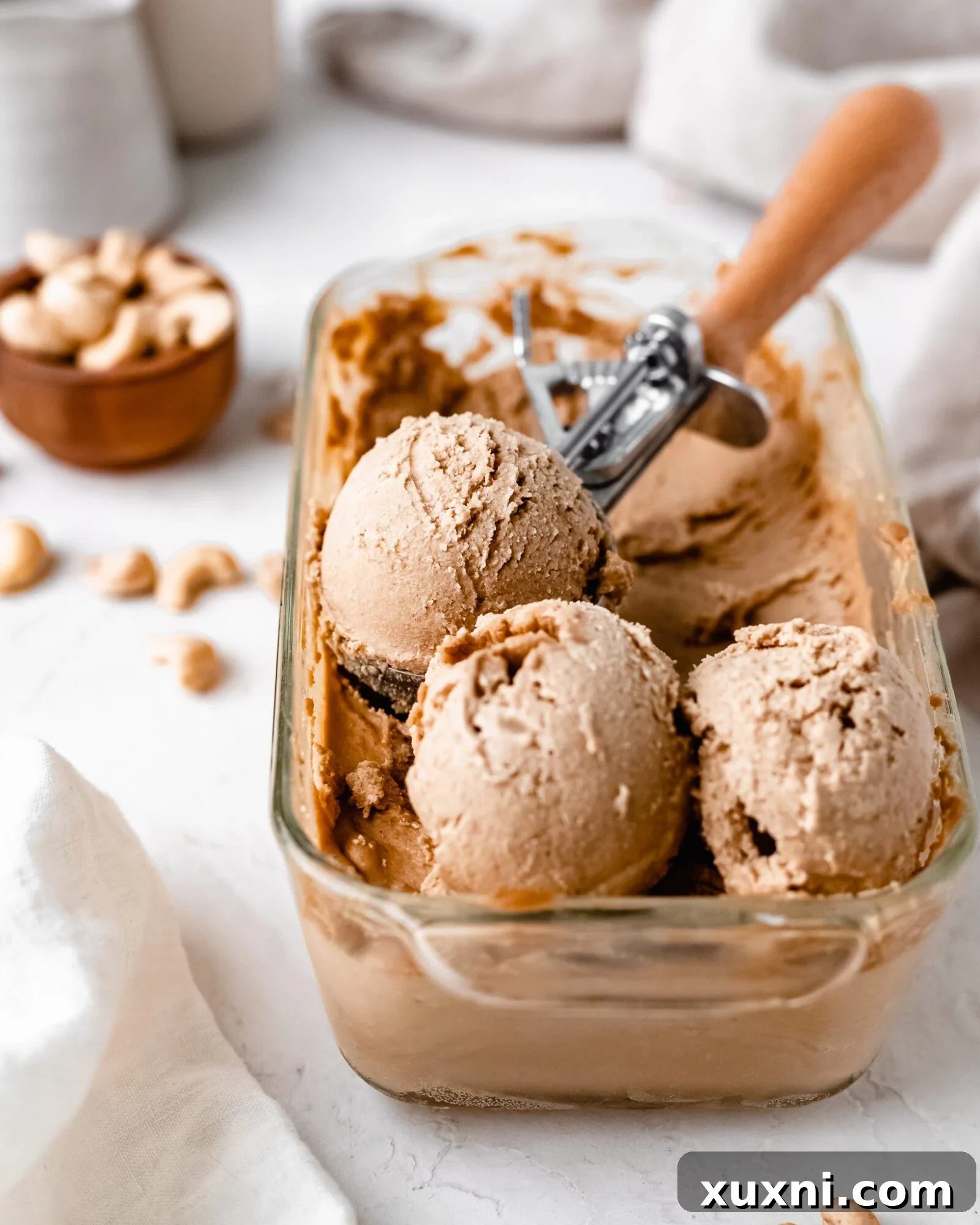 Scoops of creamy vegan vanilla ice cream in a white bowl, garnished with a sprig.