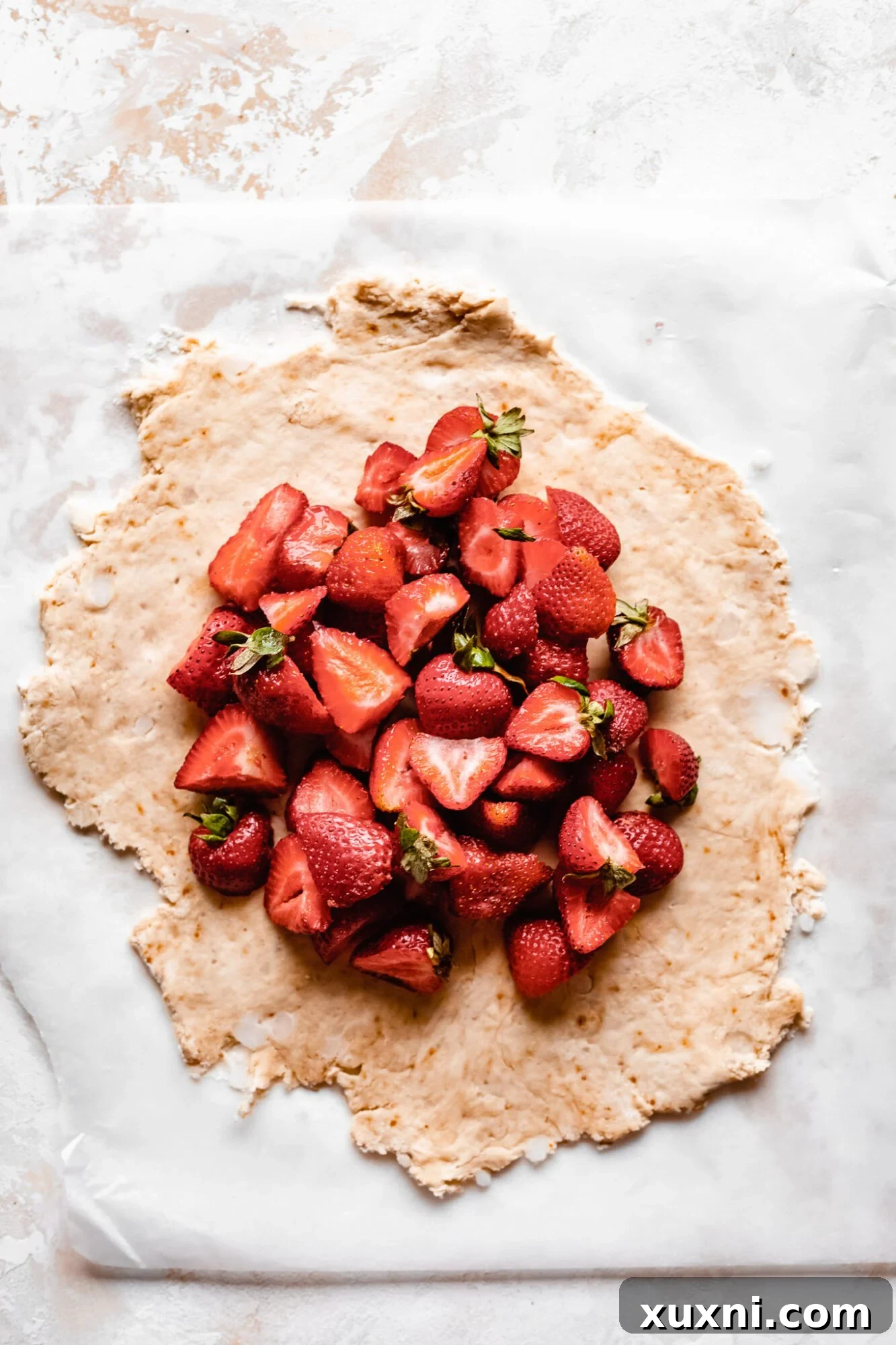 Rolled-out pie dough with sliced strawberries neatly arranged in the center, leaving a border