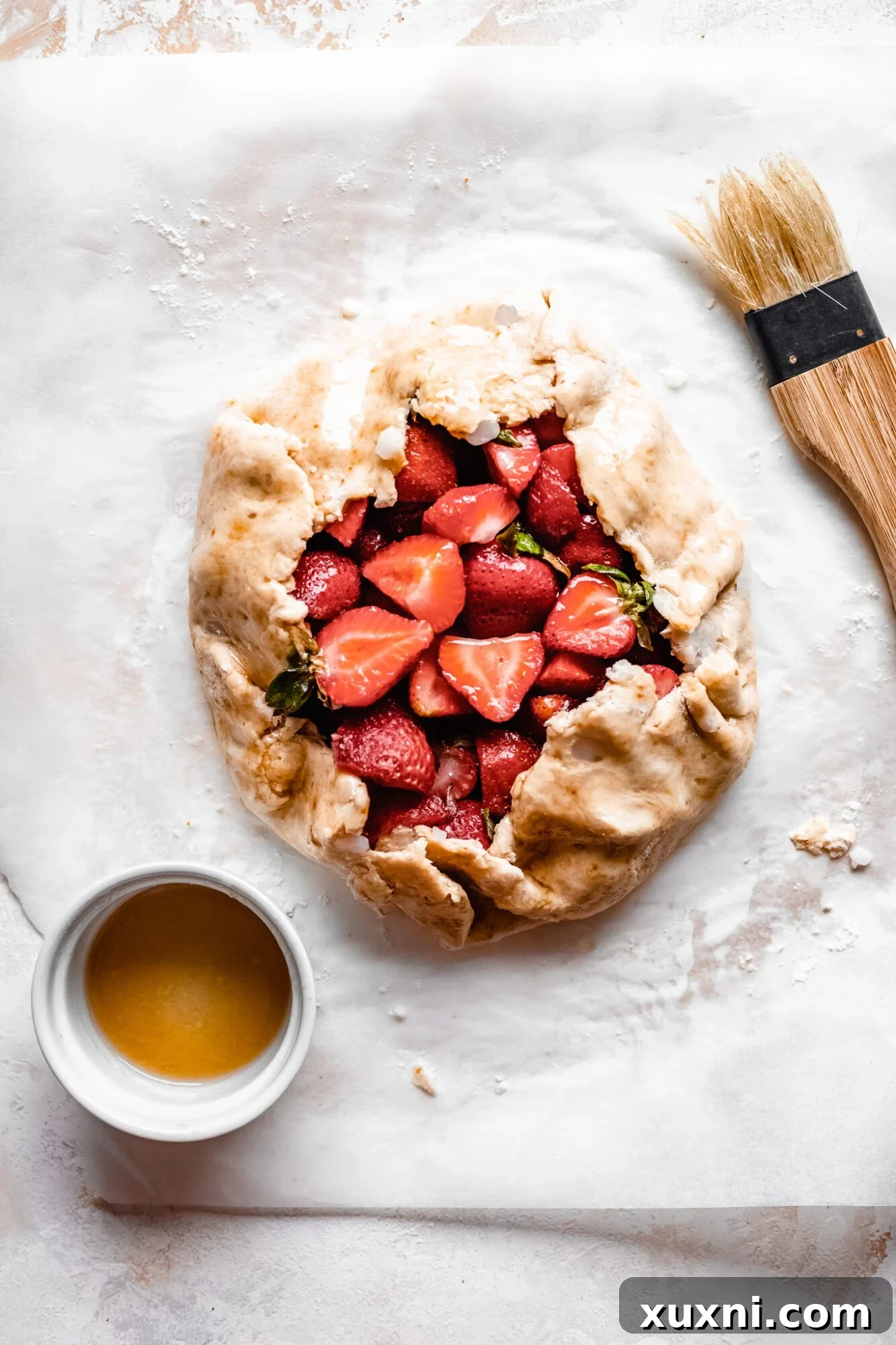 Unbaked strawberry galette on parchment paper, with the crust edges folded over the fruit