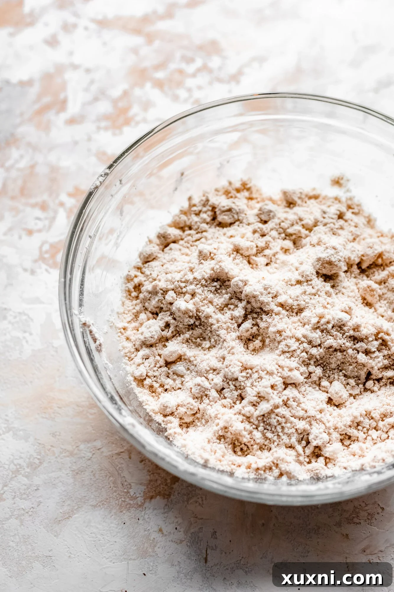 Close-up of flour and coconut oil mixture in a bowl, showing the sandy, crumbly texture after cutting in the fat