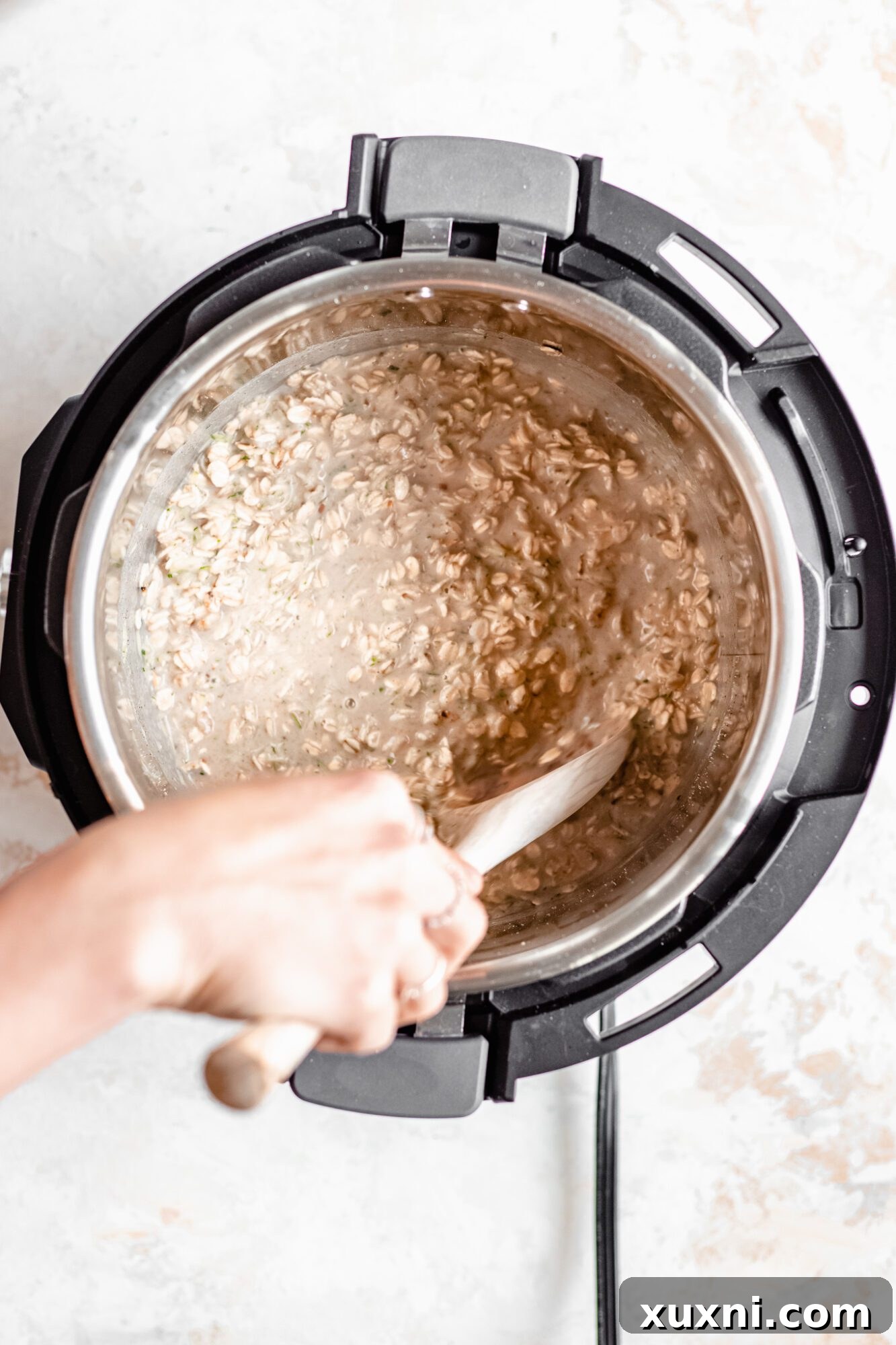 Instant Pot Protein Packed Vegan Zucchini Oatmeal 9 hand mixing wet ingredients like milk, zucchini, and maple syrup into oats in an Instant Pot