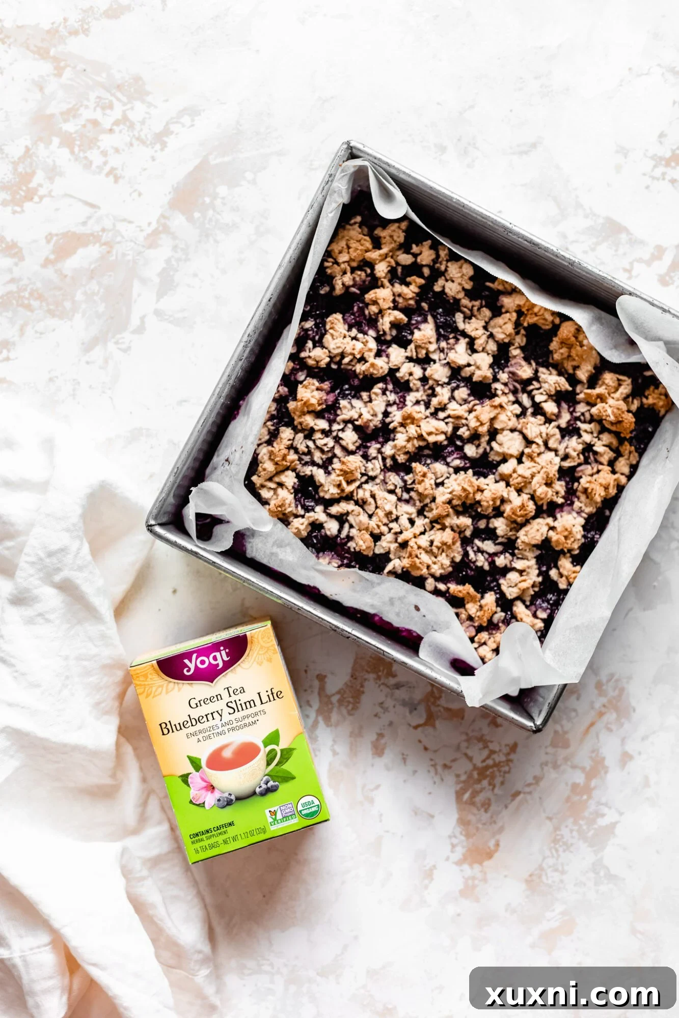 Baked healthy blueberry crumble bars in a baking dish, with a Yogi Tea box nearby.