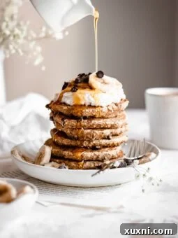 hand pouring maple syrup over chocolate chip pancakes