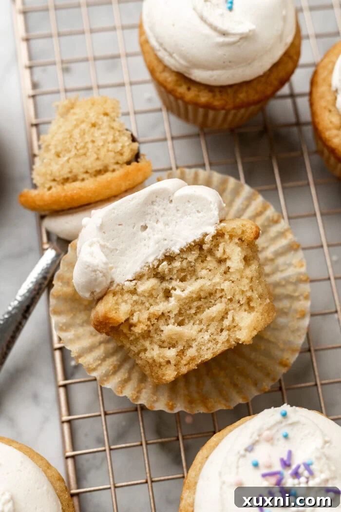 A close-up of a bitten vegan vanilla cupcake, revealing the moist interior and creamy frosting