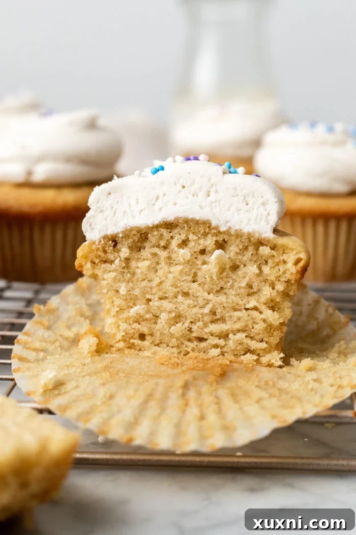 A perfectly sliced vegan vanilla cupcake with frosting, showcasing its light and airy texture