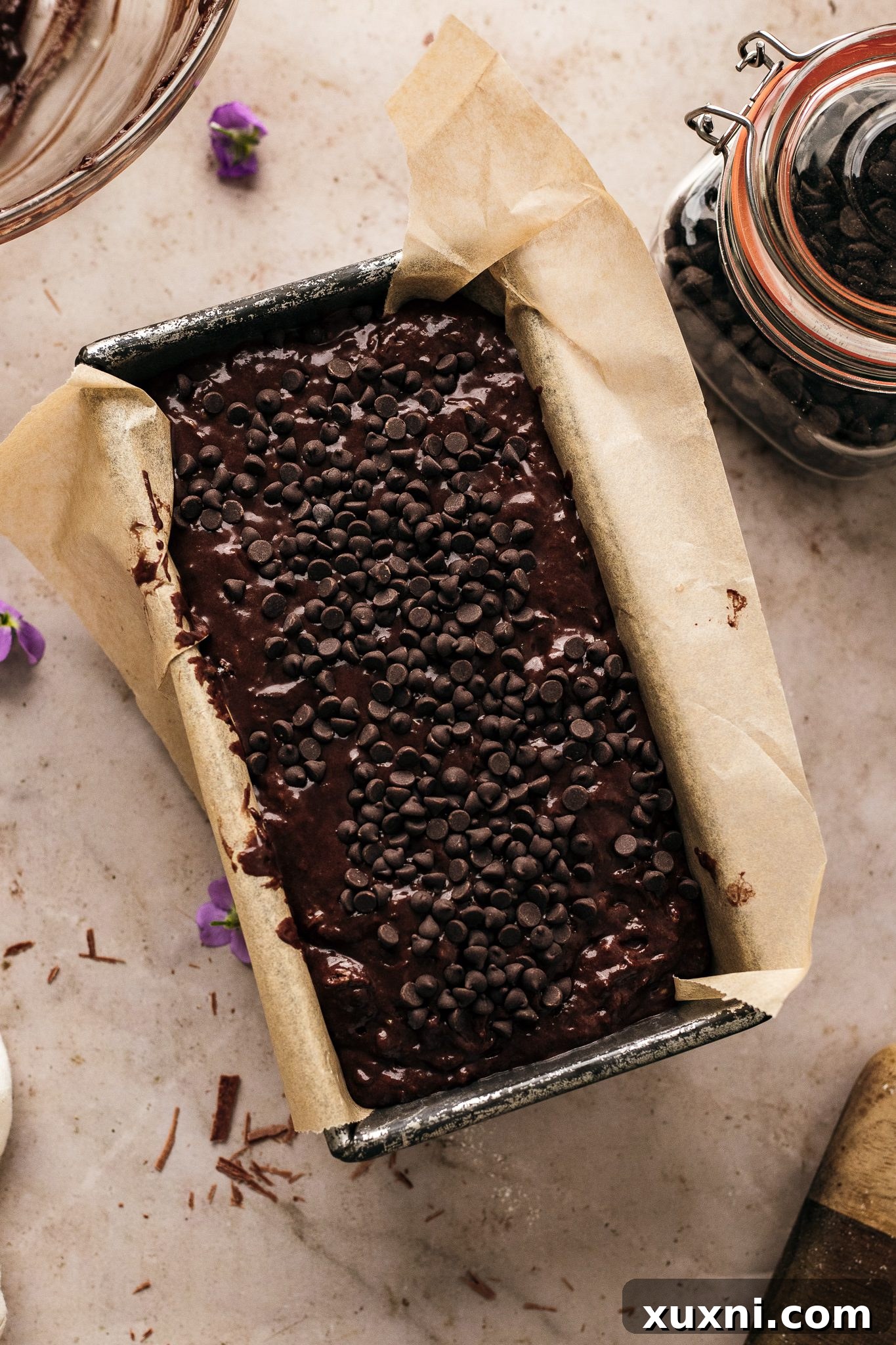 Unbaked vegan zucchini bread batter in a loaf pan, topped with extra chocolate chips, ready for the oven.