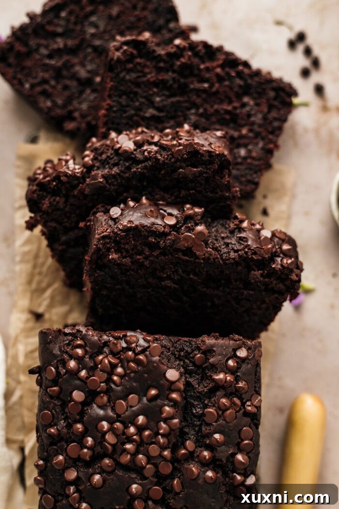 Several slices of rich vegan chocolate zucchini bread arranged on a cutting board, showcasing its moist texture and chocolate chips.