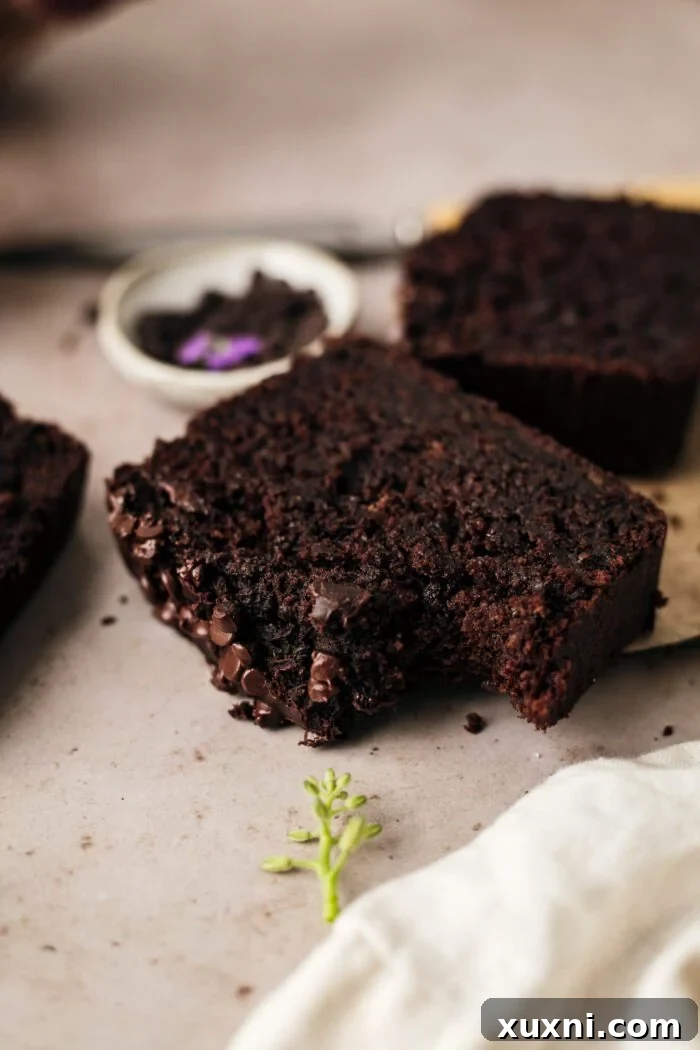 A single slice of vegan chocolate zucchini bread with a bite taken out, highlighting its rich, moist interior and deliciousness.