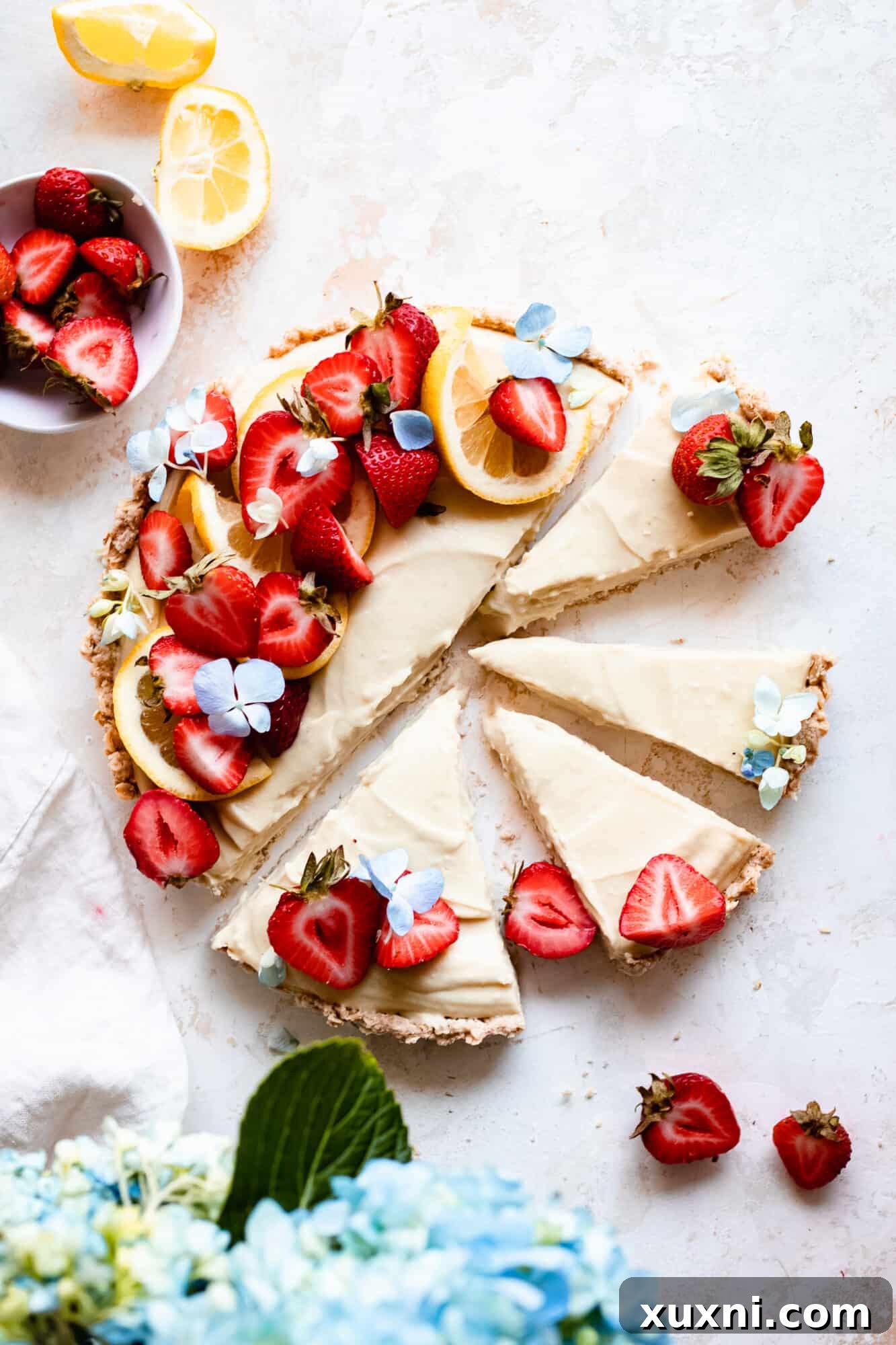 A beautifully presented slice of lemon tart with strawberries next to a delicate hydrangea flower, capturing a summer aesthetic.