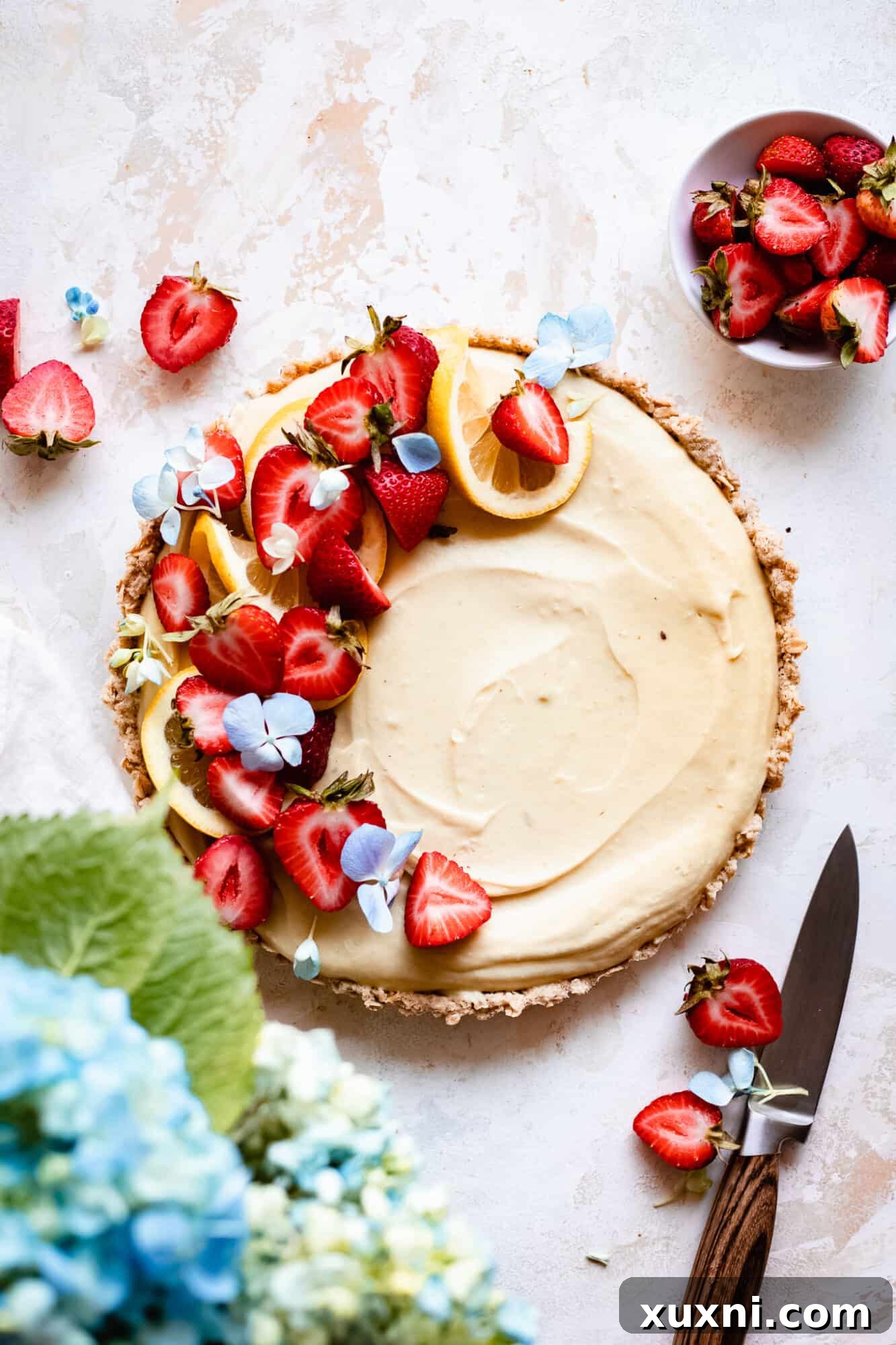 A beautiful whole vegan lemon custard tart, generously topped with fresh strawberries, ready to be served.