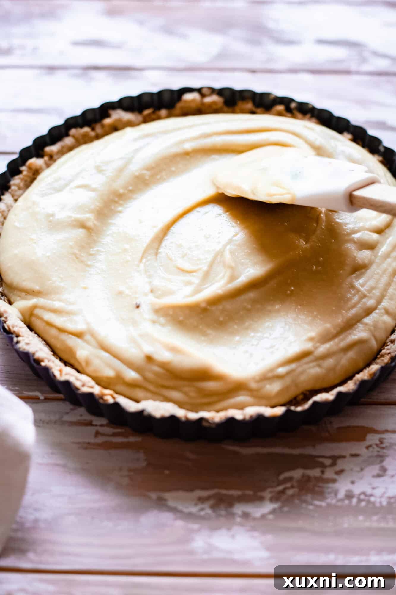 A spatula smearing the rich, yellow vegan lemon custard filling in a bowl, showing its thick and smooth consistency.