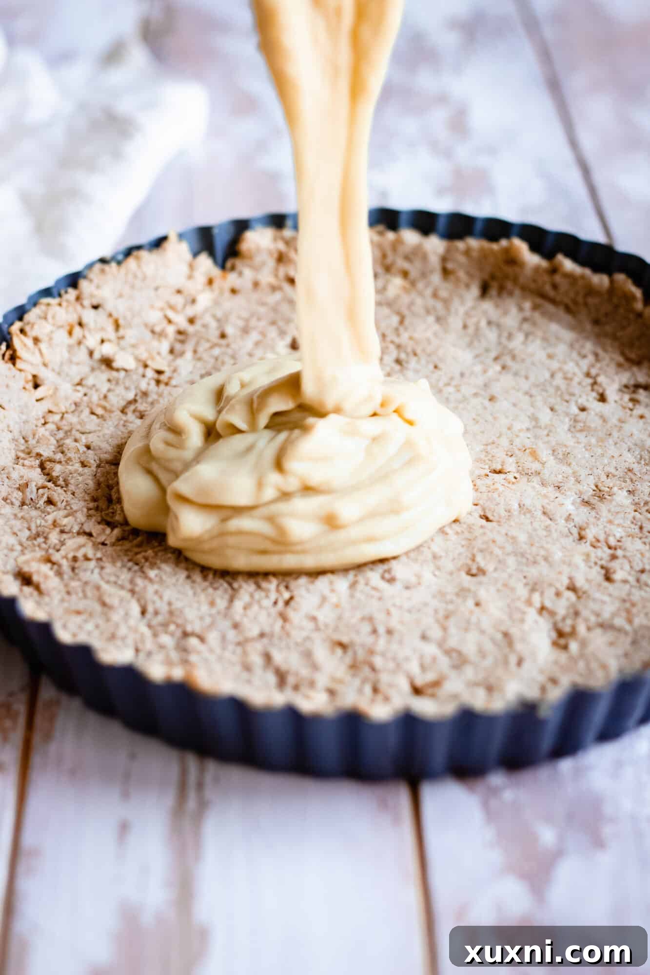 Pouring the creamy vegan lemon custard filling into the pre-baked gluten-free oat crust in a tart pan.