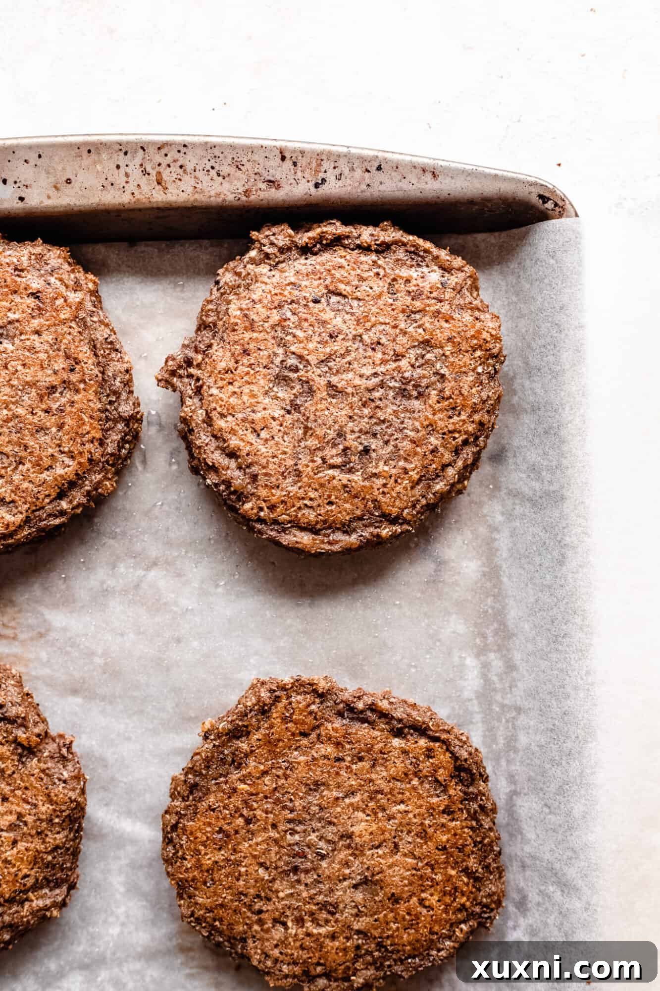 Partially baked vegan veggie burger patties neatly arranged on a parchment-lined baking sheet.
